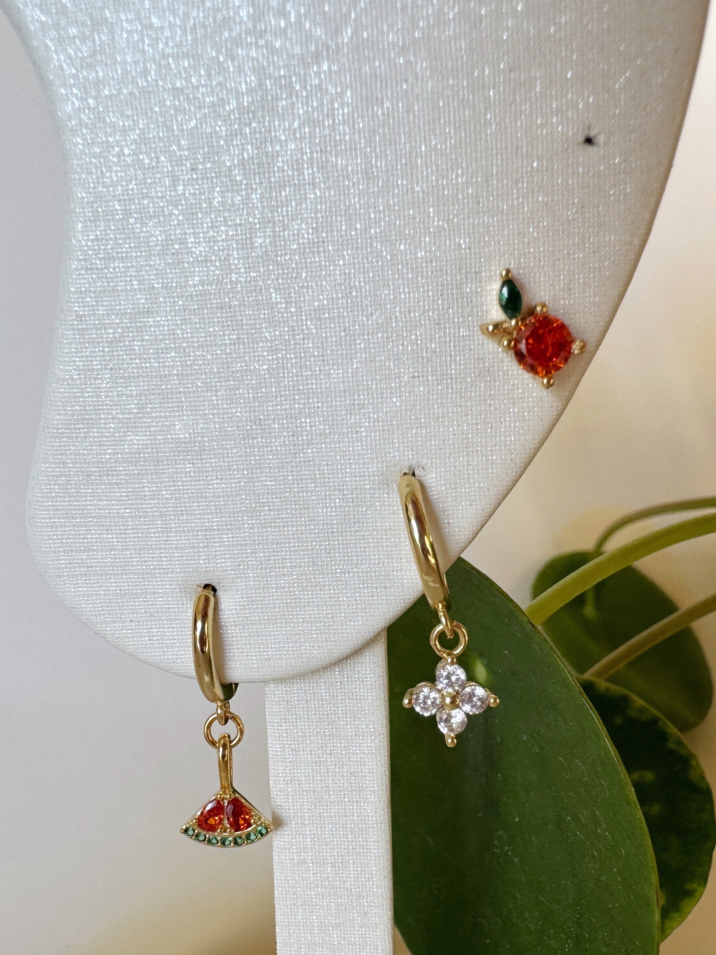 Pair of earrings on a white stand with green leaves in the background