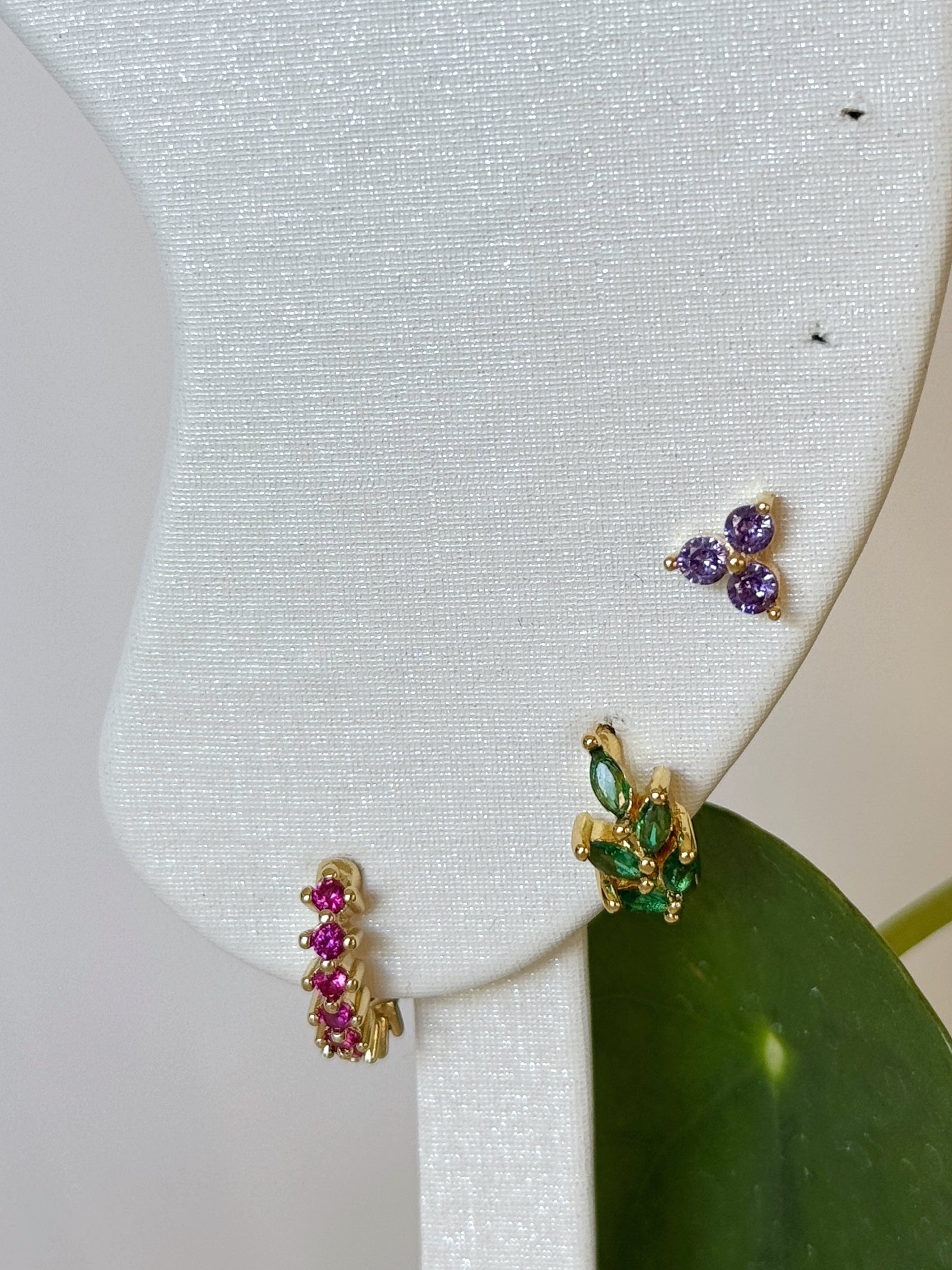 Gold earrings with green, pink and lavender gemstones on a white background