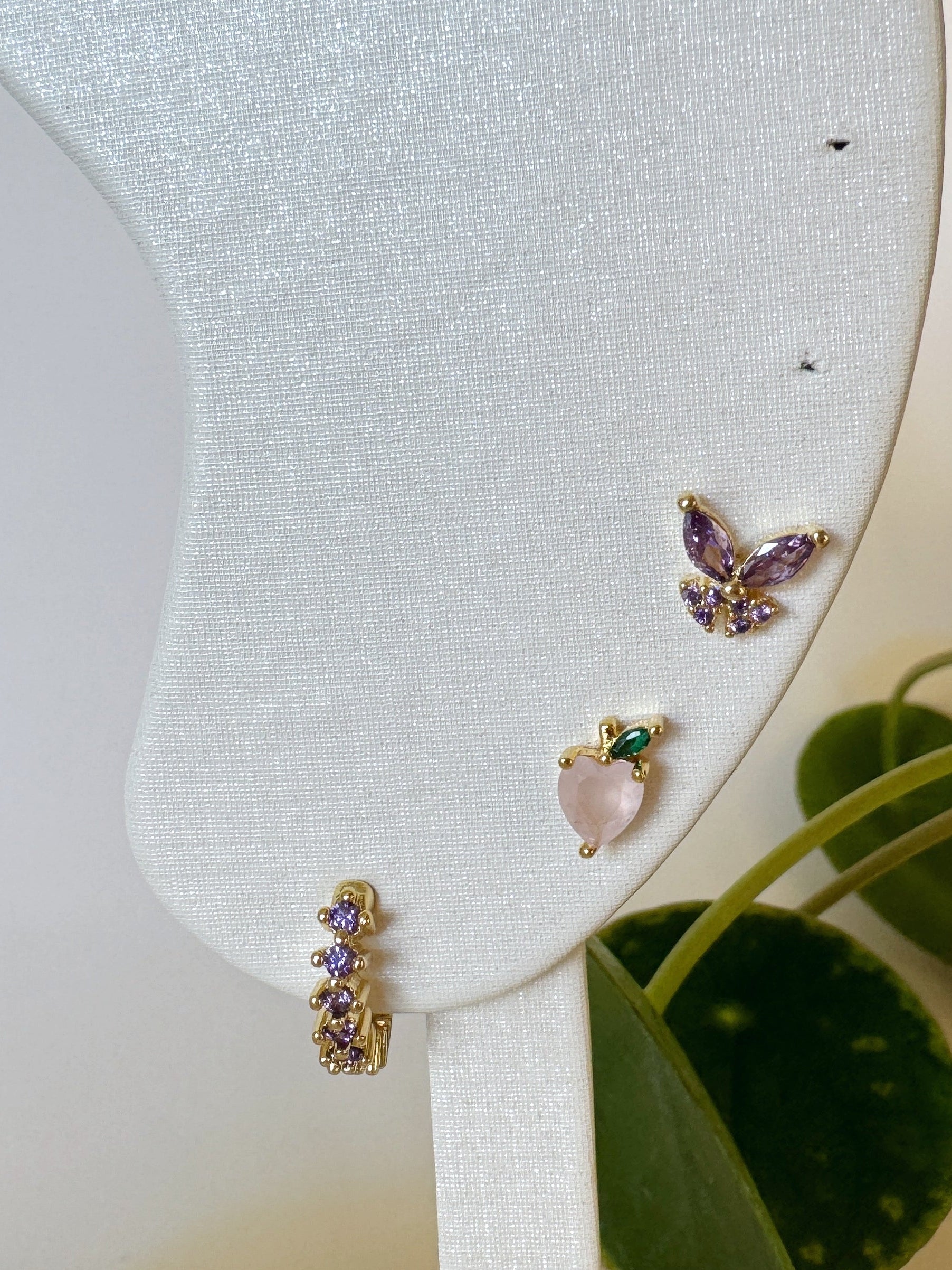 Butterfly-shaped waterproof earrings on a white stand with green leaves in the background
