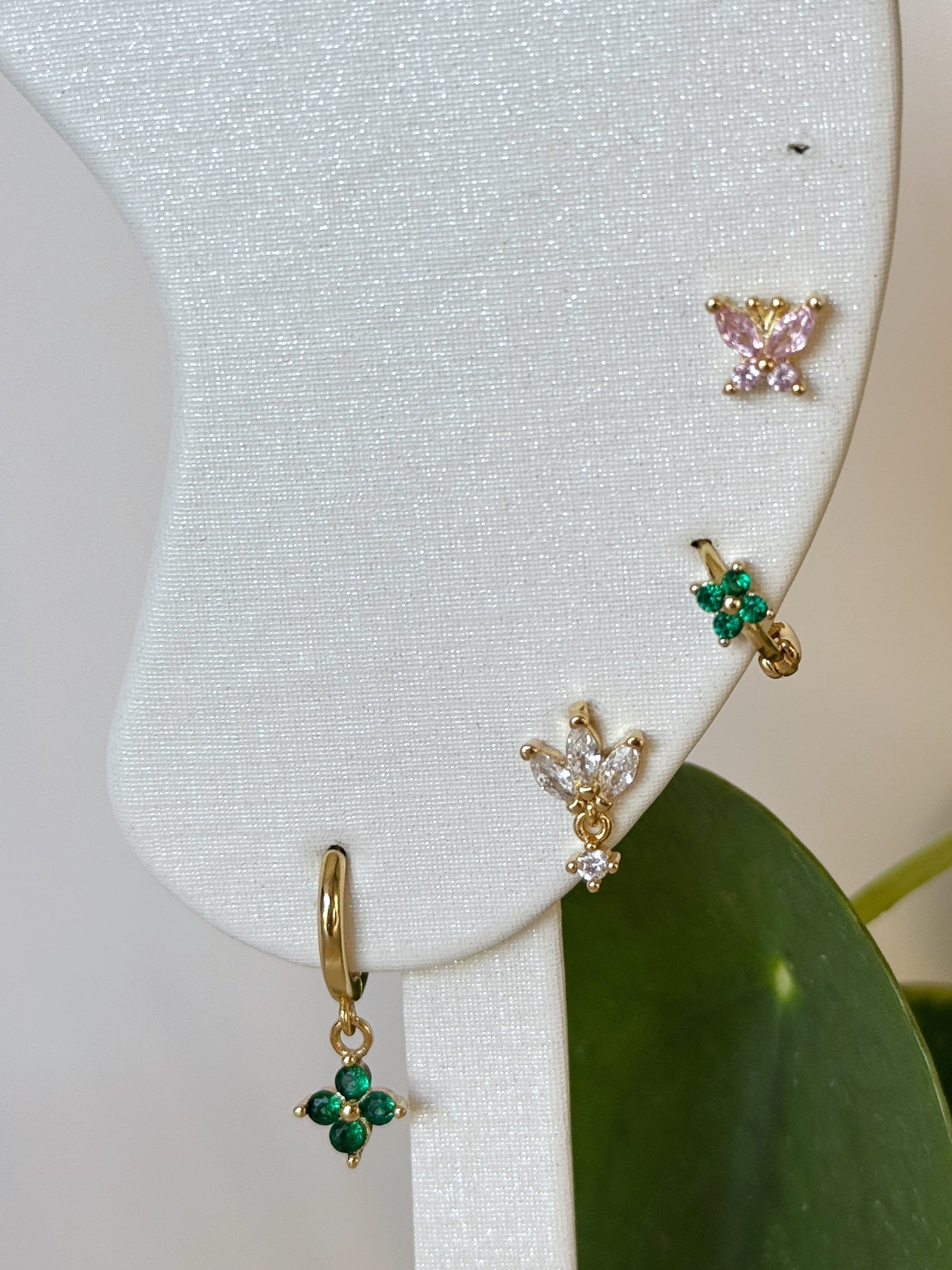Gold and green stud and hoop waterproof earrings on a white card with green leaves in the background