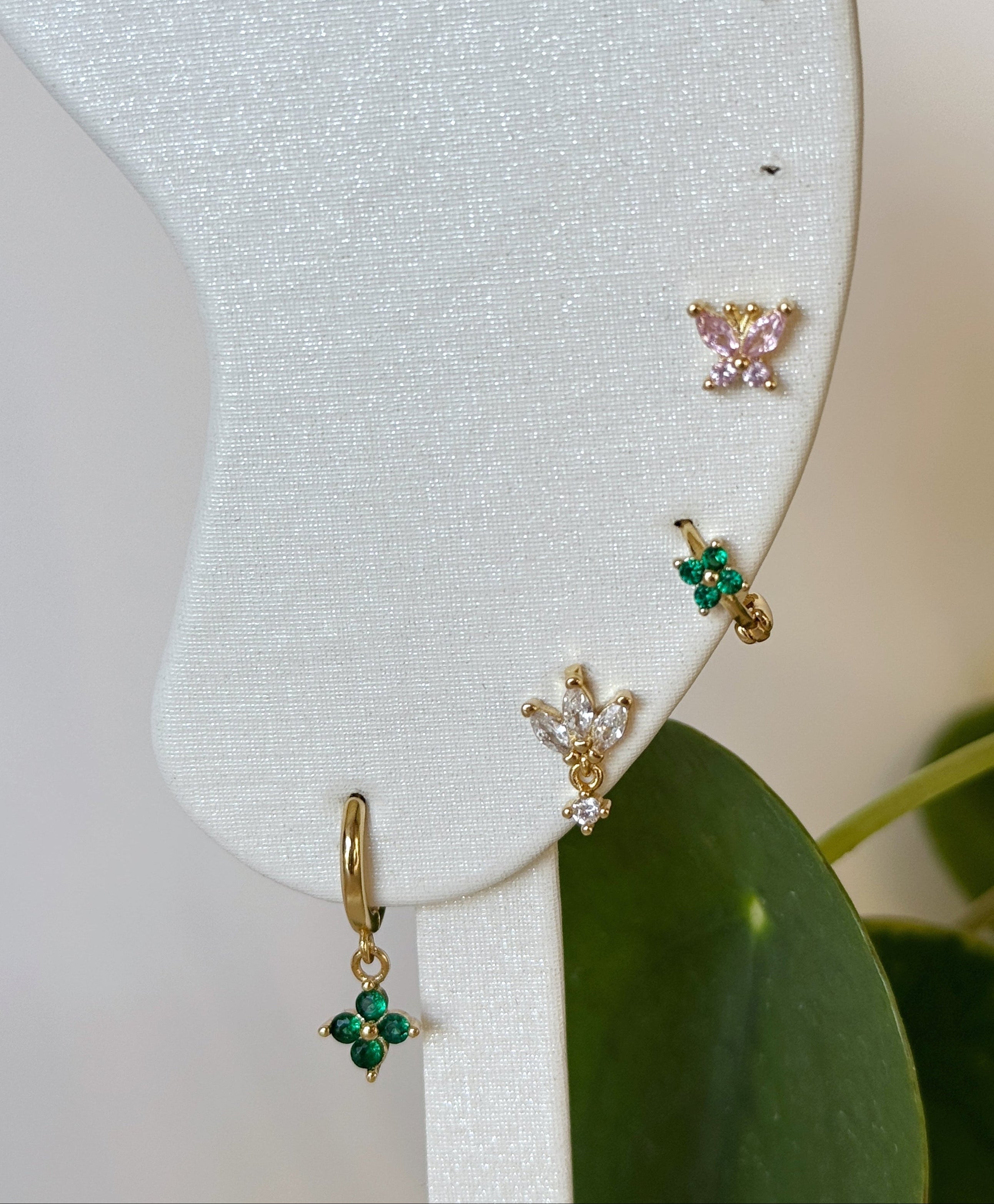 Gold and silver earrings on a white card with green leaves in the background