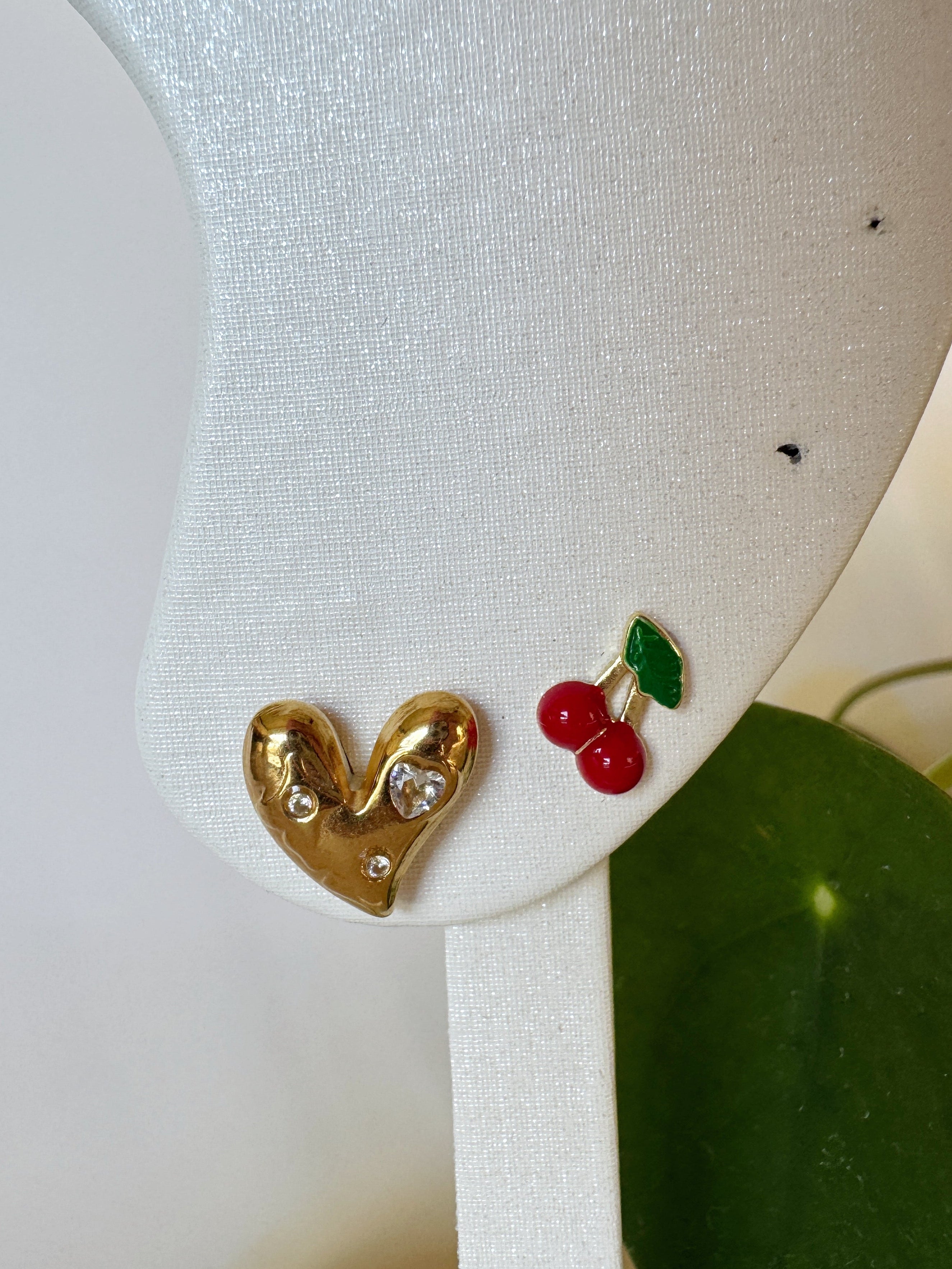 Heart-shaped earrings with red cherries on a white stand.