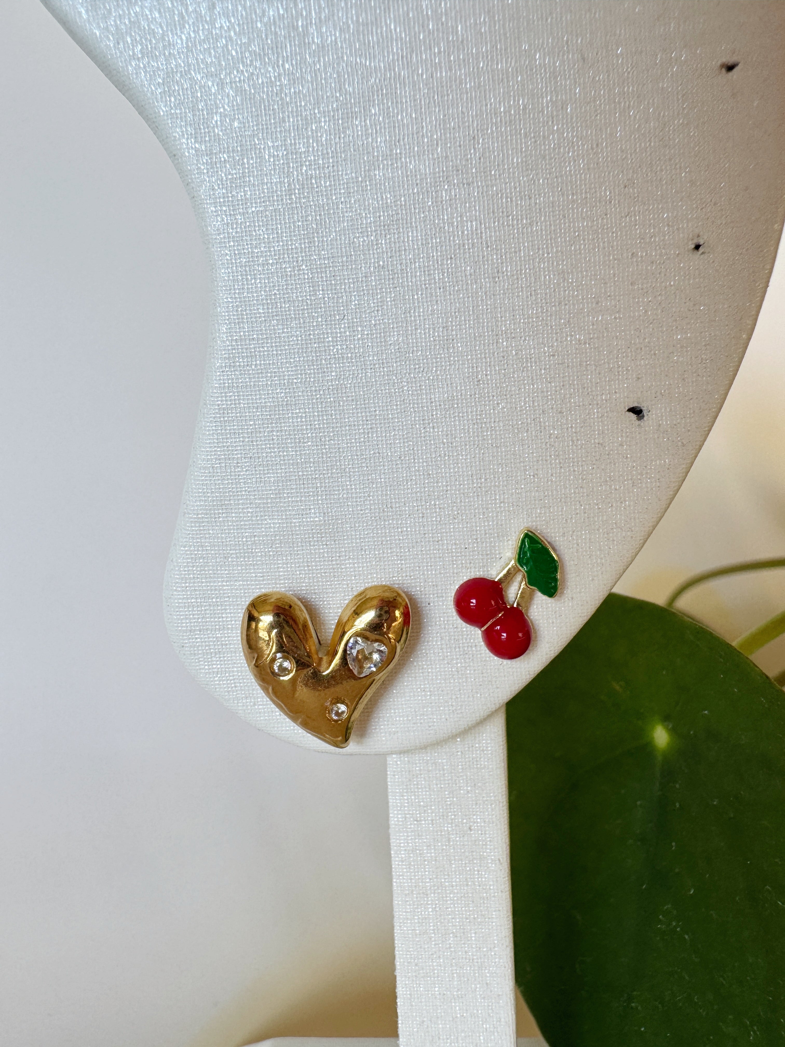 Heart-shaped earrings with red cherries on a white stand.