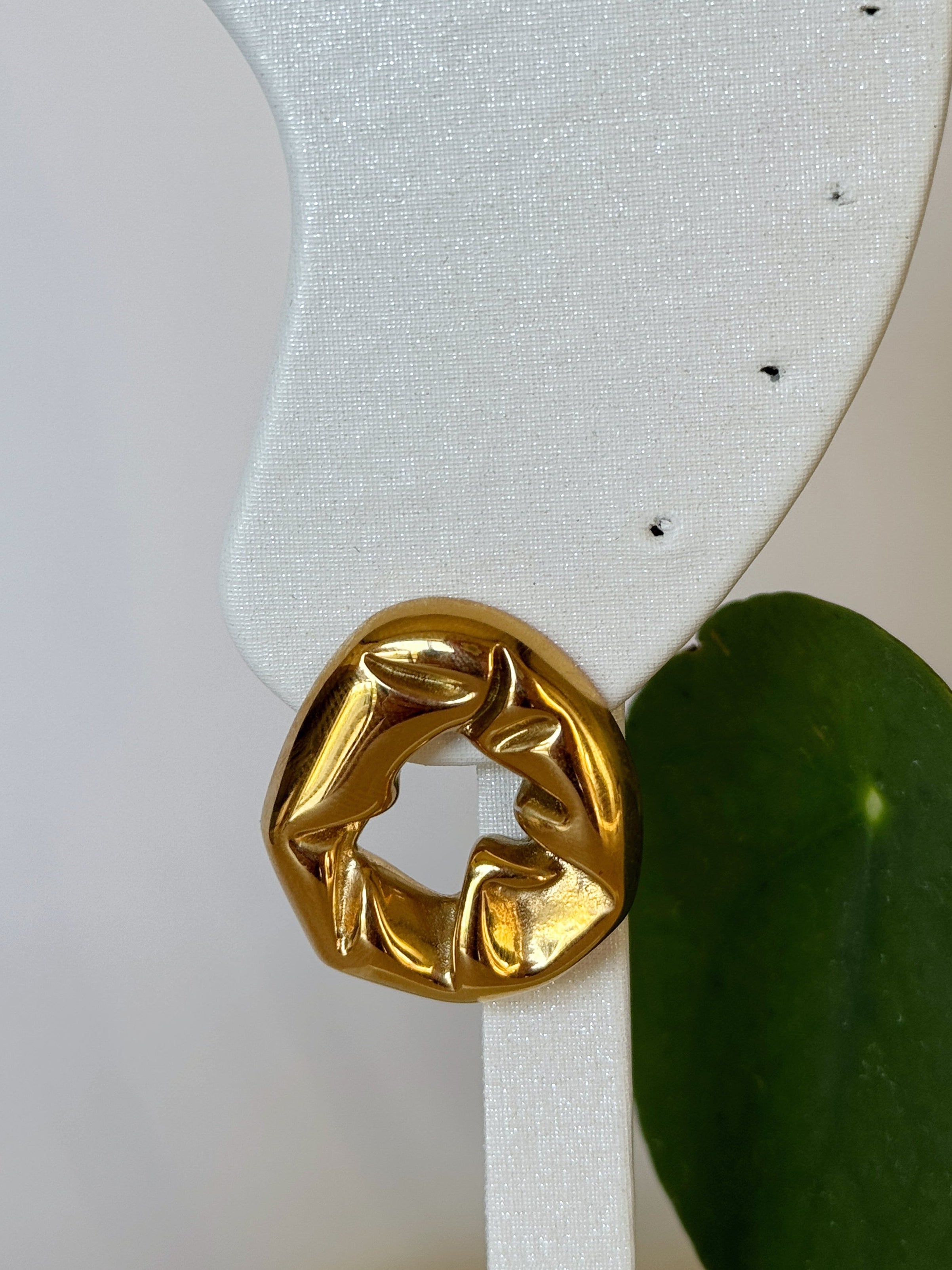 Big gold earring on a white stand with a green leaf in the background