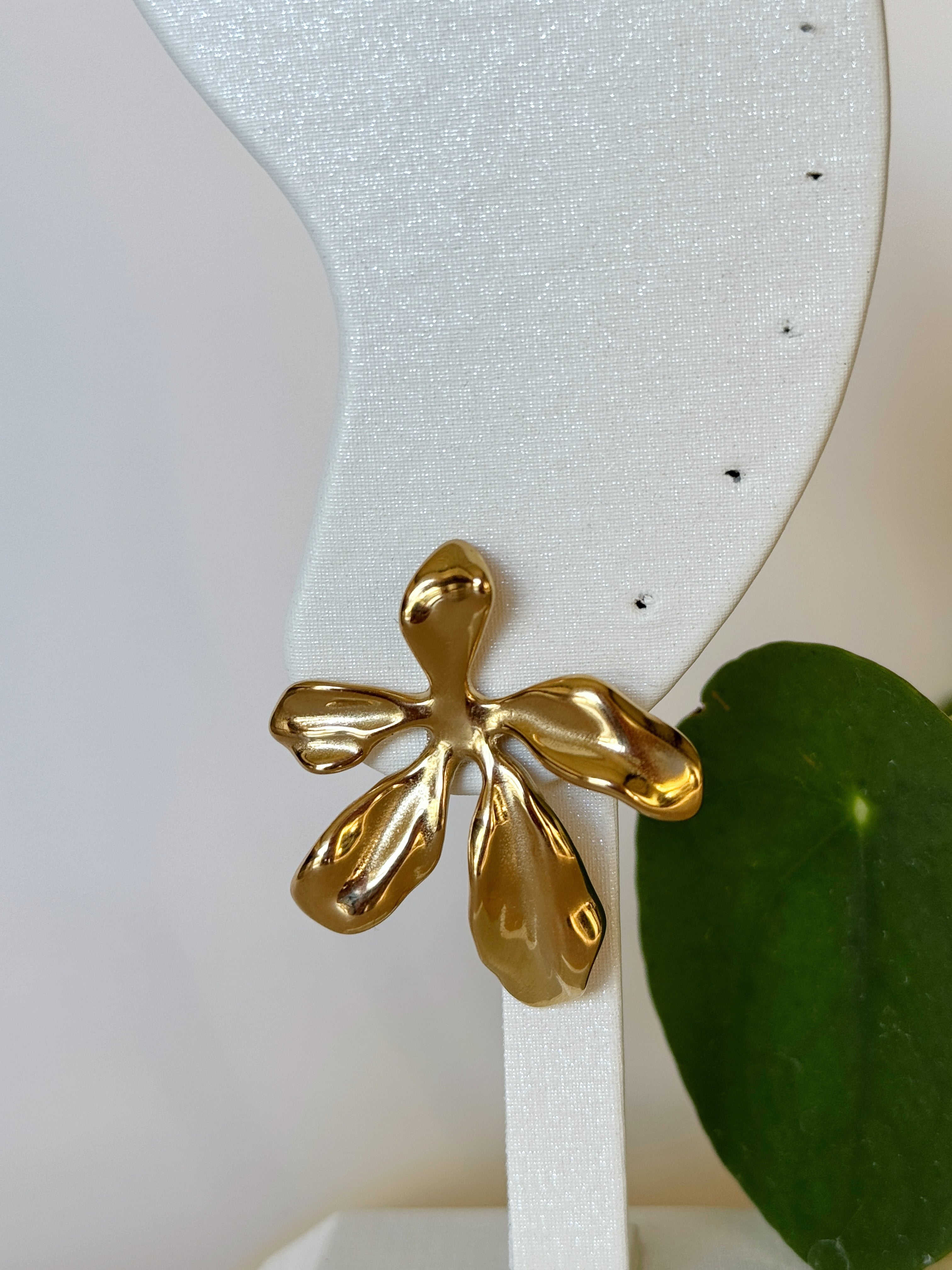 Big gold girly flower earring on a white stand with a green leaf in the background