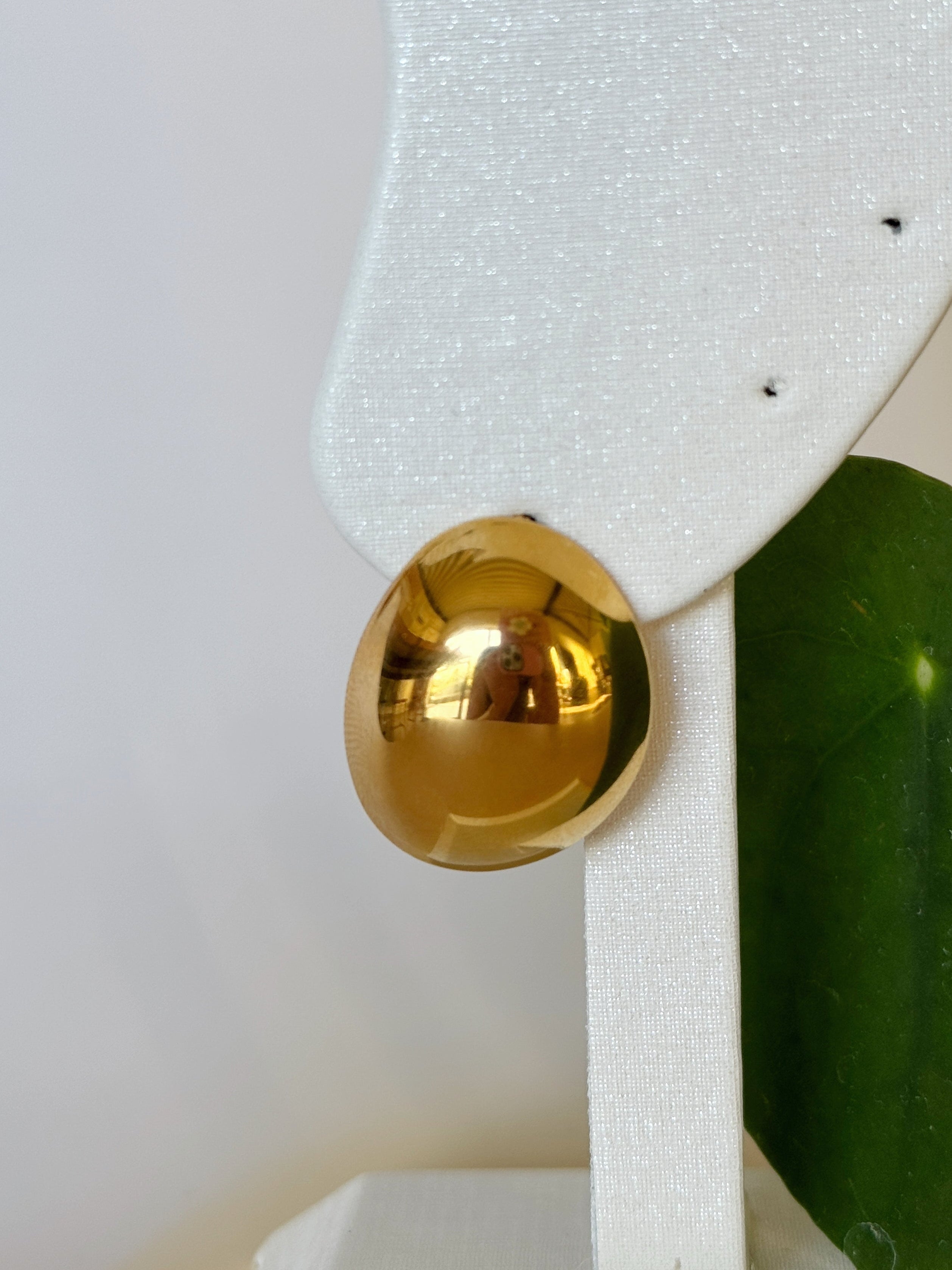 Classic stainless steel gold earring on a white stand with a green leaf background