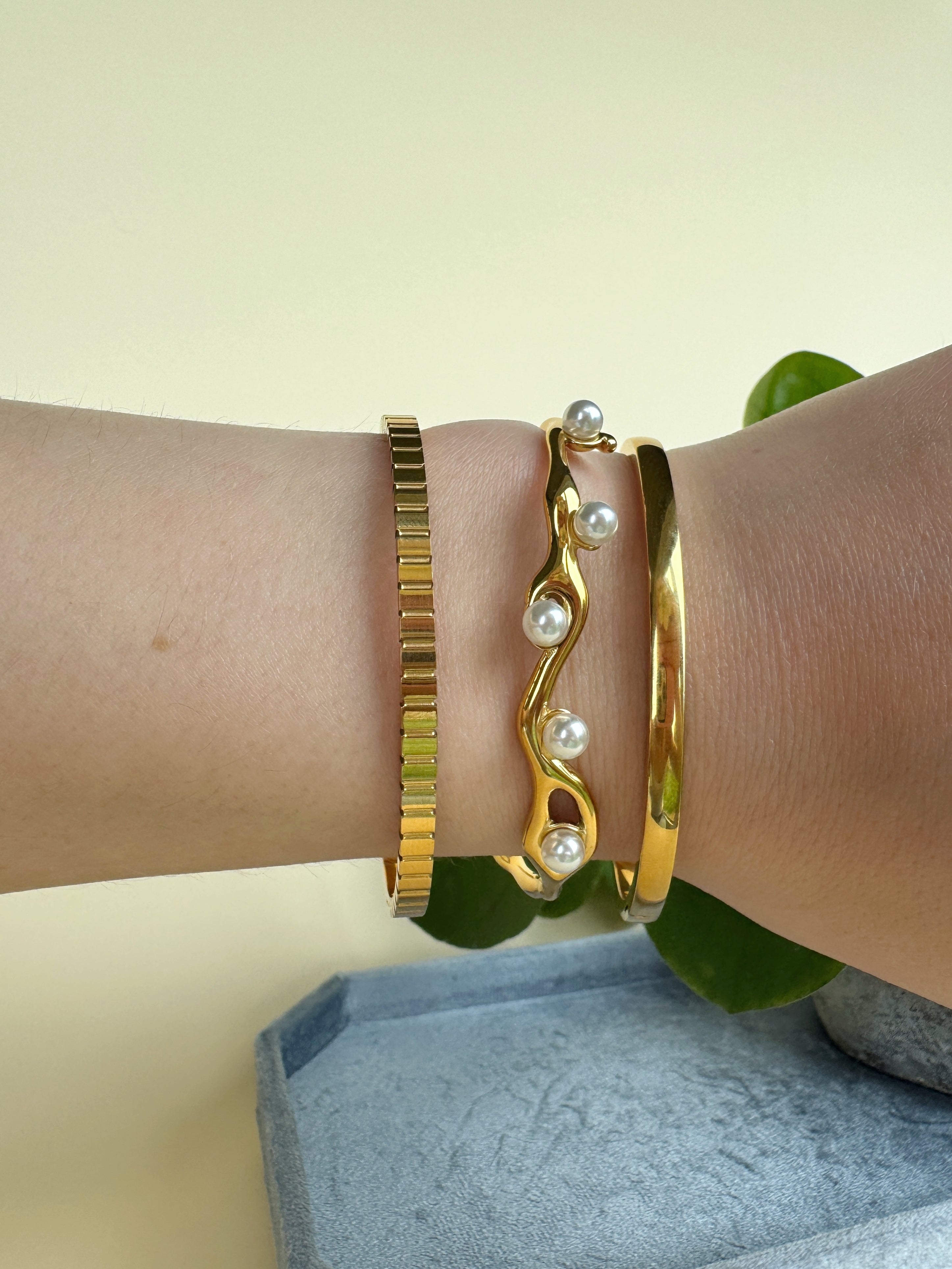 Gold bracelets with pearl accents on a wrist against a light background