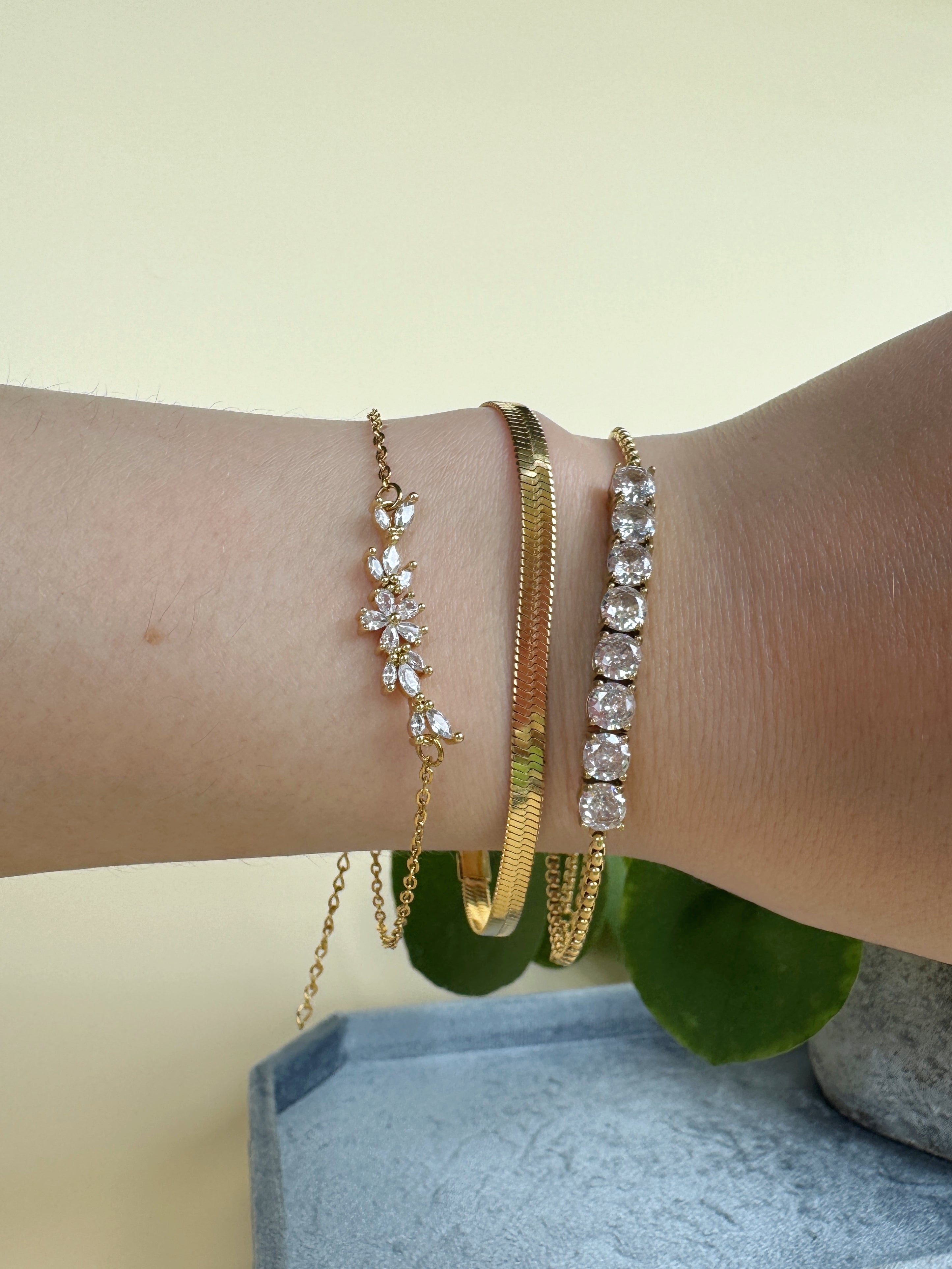 Close-up of a wrist wearing gold and diamond bracelets on a neutral background