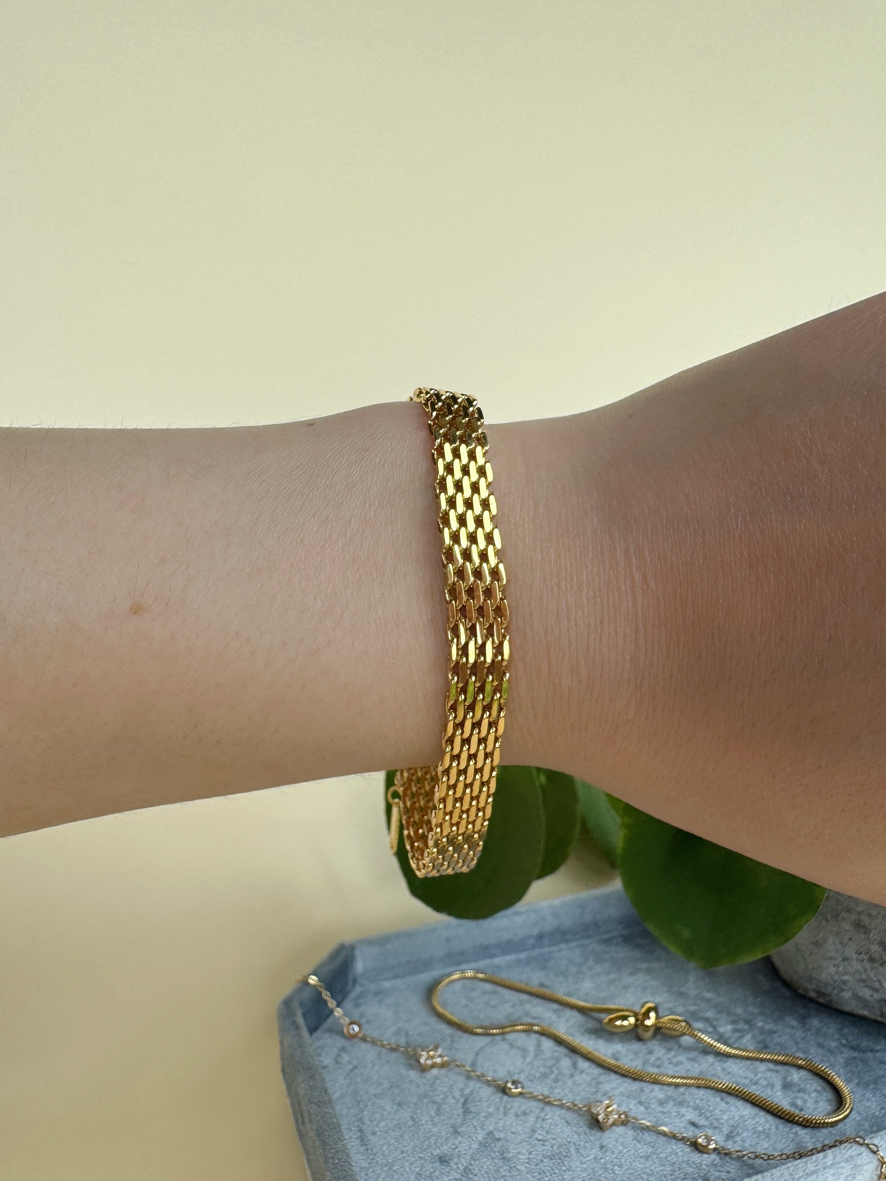 Gold chain bracelet on a wrist with a neutral background