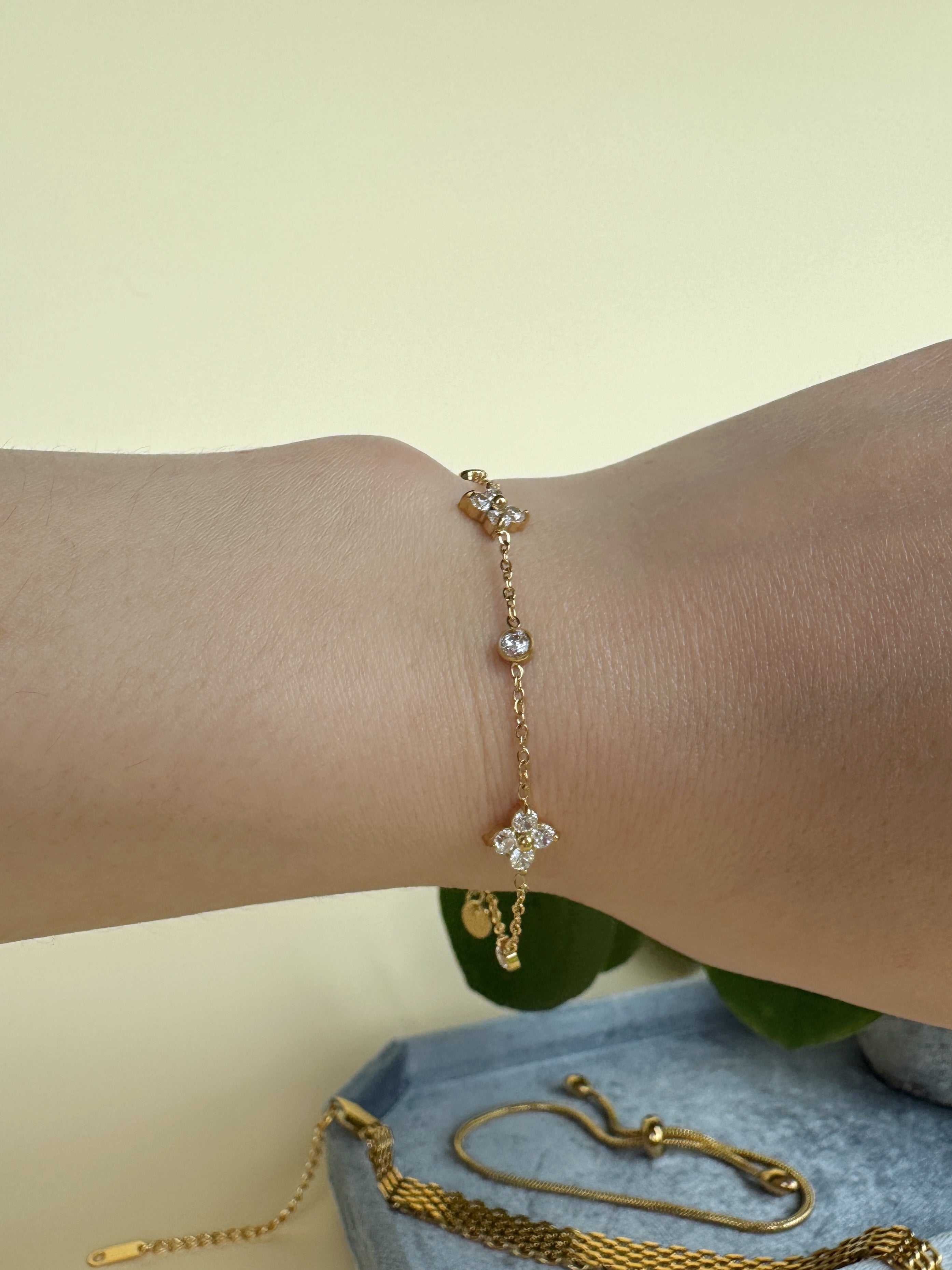 Girly gold bracelet with a floral charm on a wrist against a light background