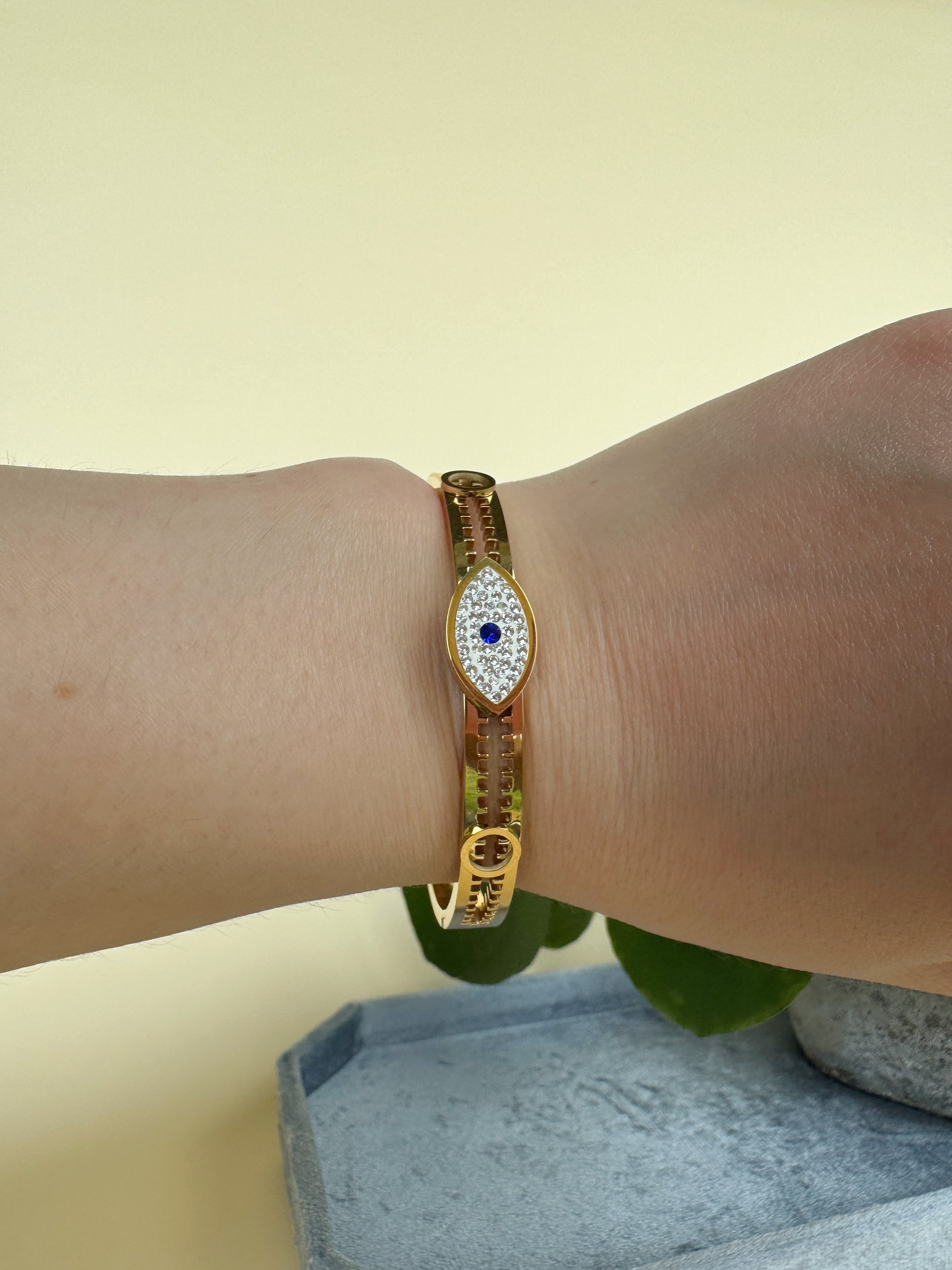 Gold bracelet with an evil eye design worn on a wrist against a neutral background for protecing energy and good luck