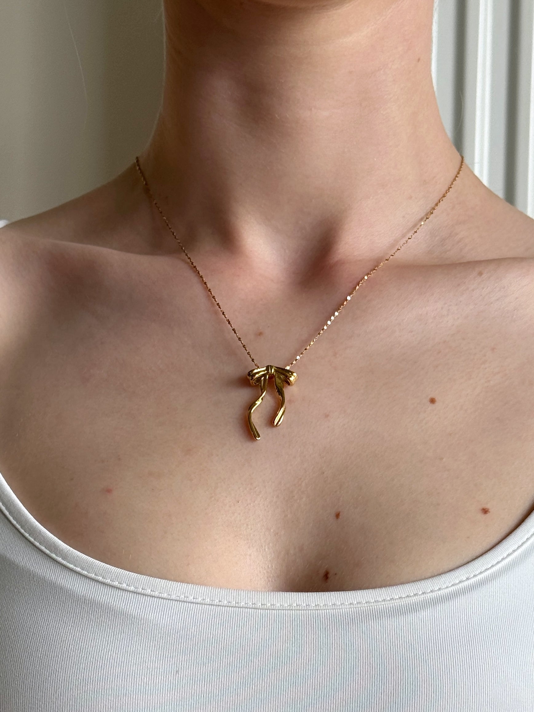 Gold necklace with a bow pendant on a person wearing a white top.