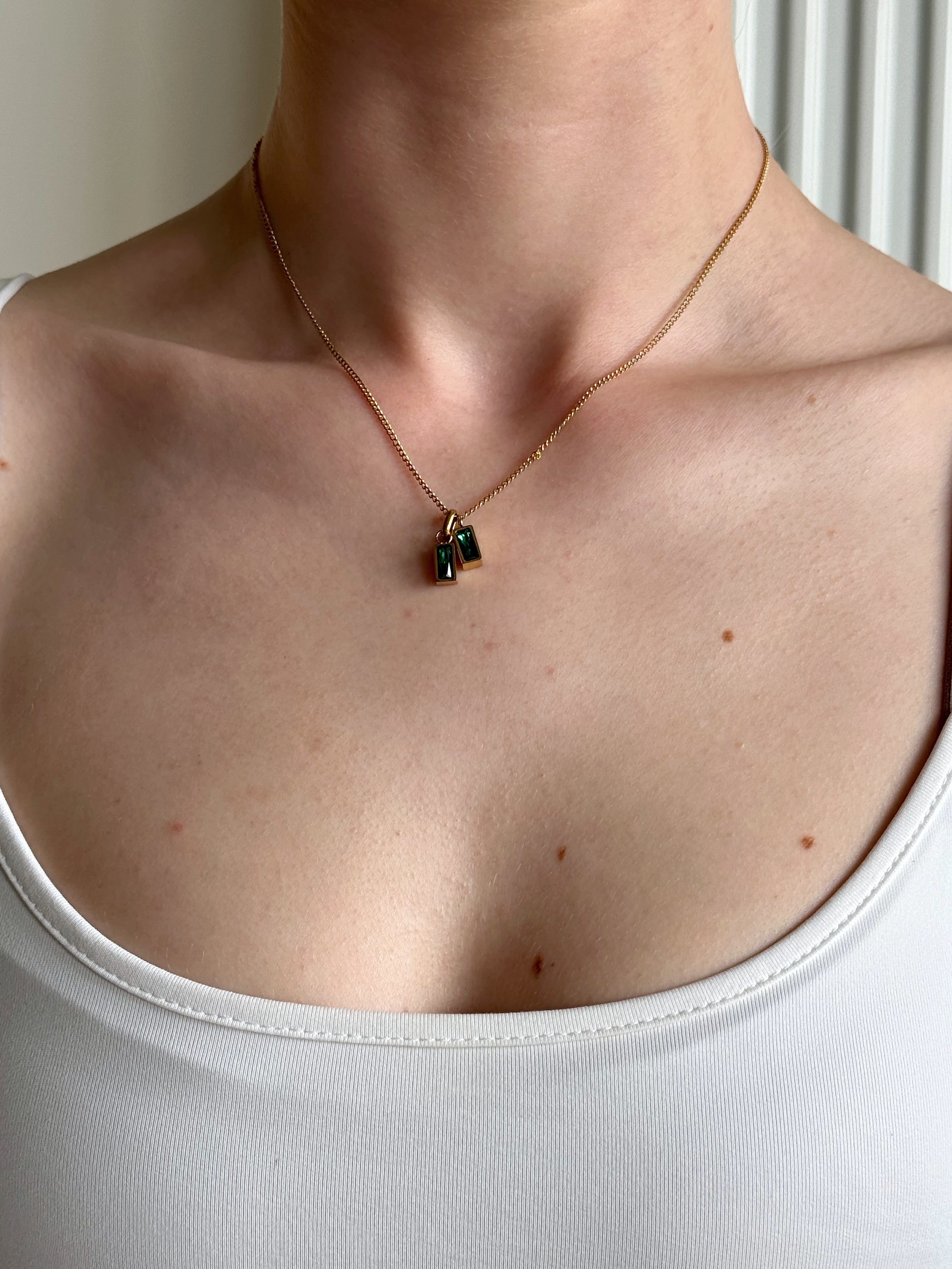 Necklace with a green double pendant worn by a girl in a white top.