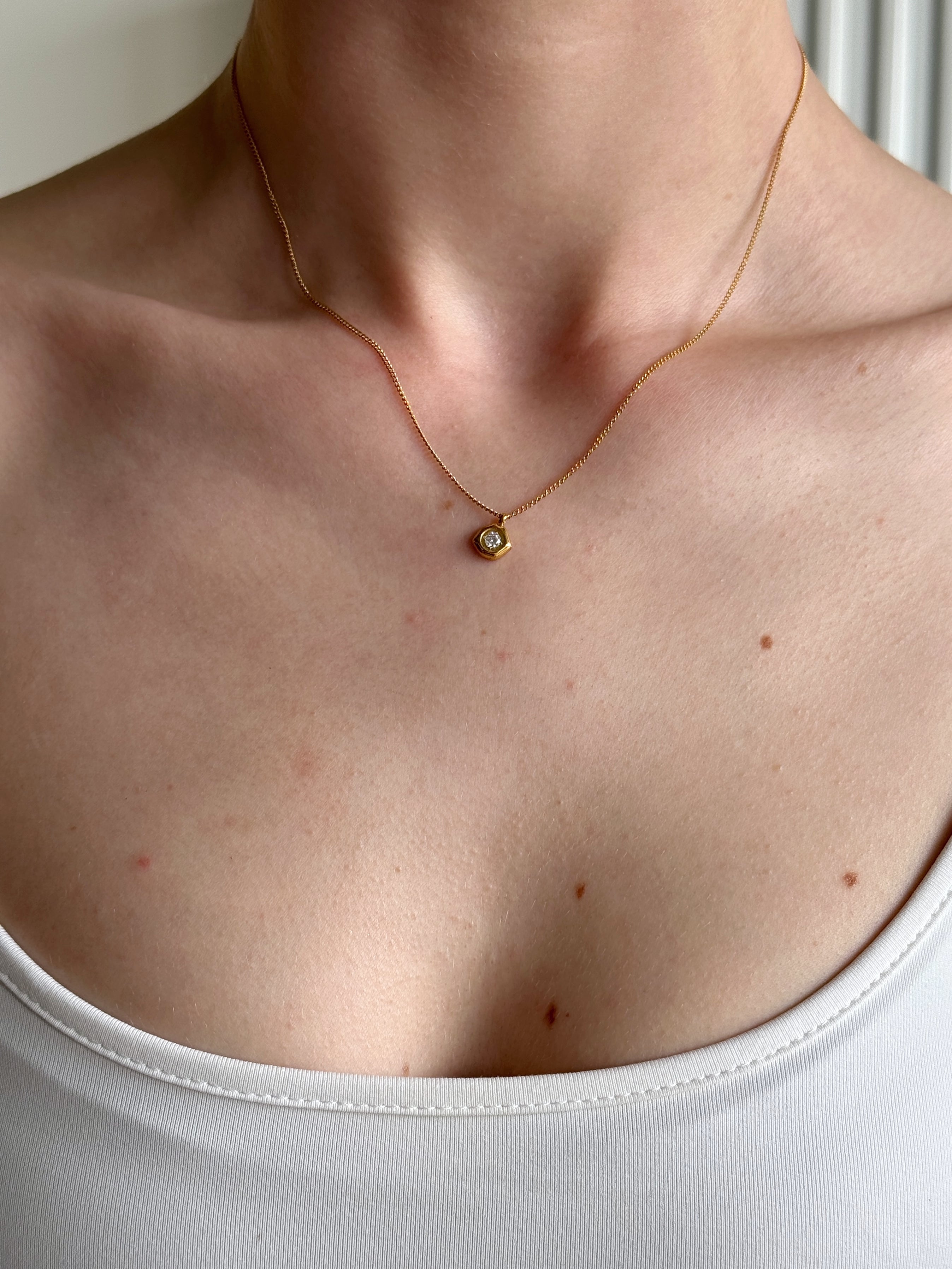Necklace with a small pendant worn by a person against a neutral background