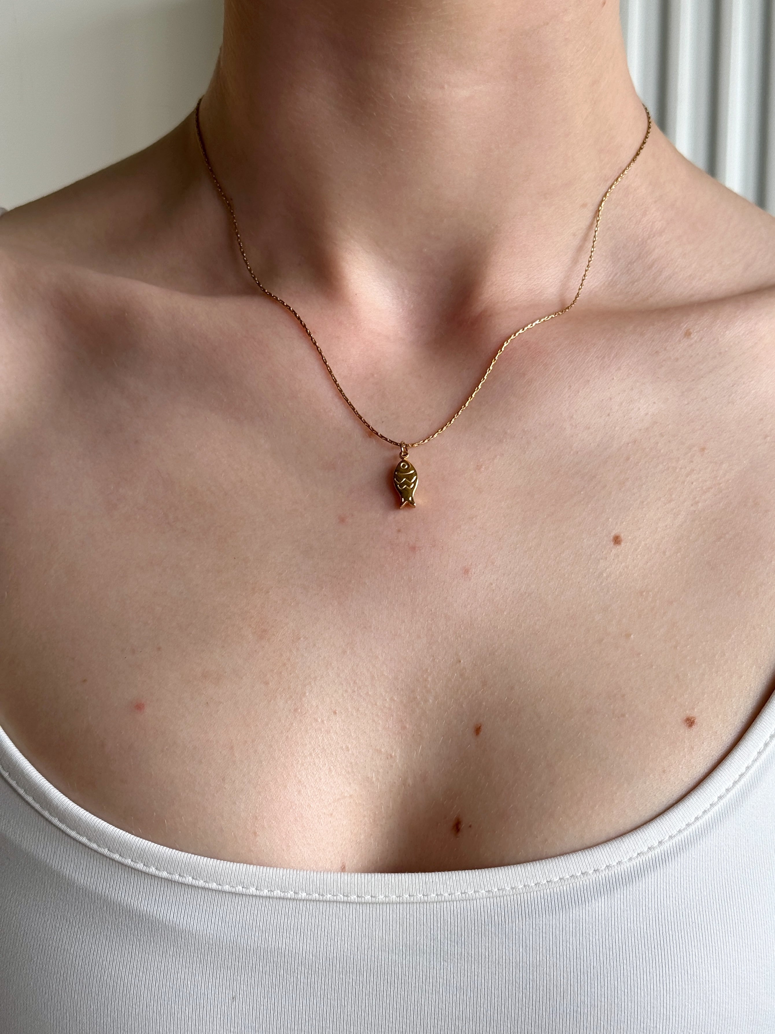 Gold waterproof necklace with a small fish pendant on a person wearing a white top.