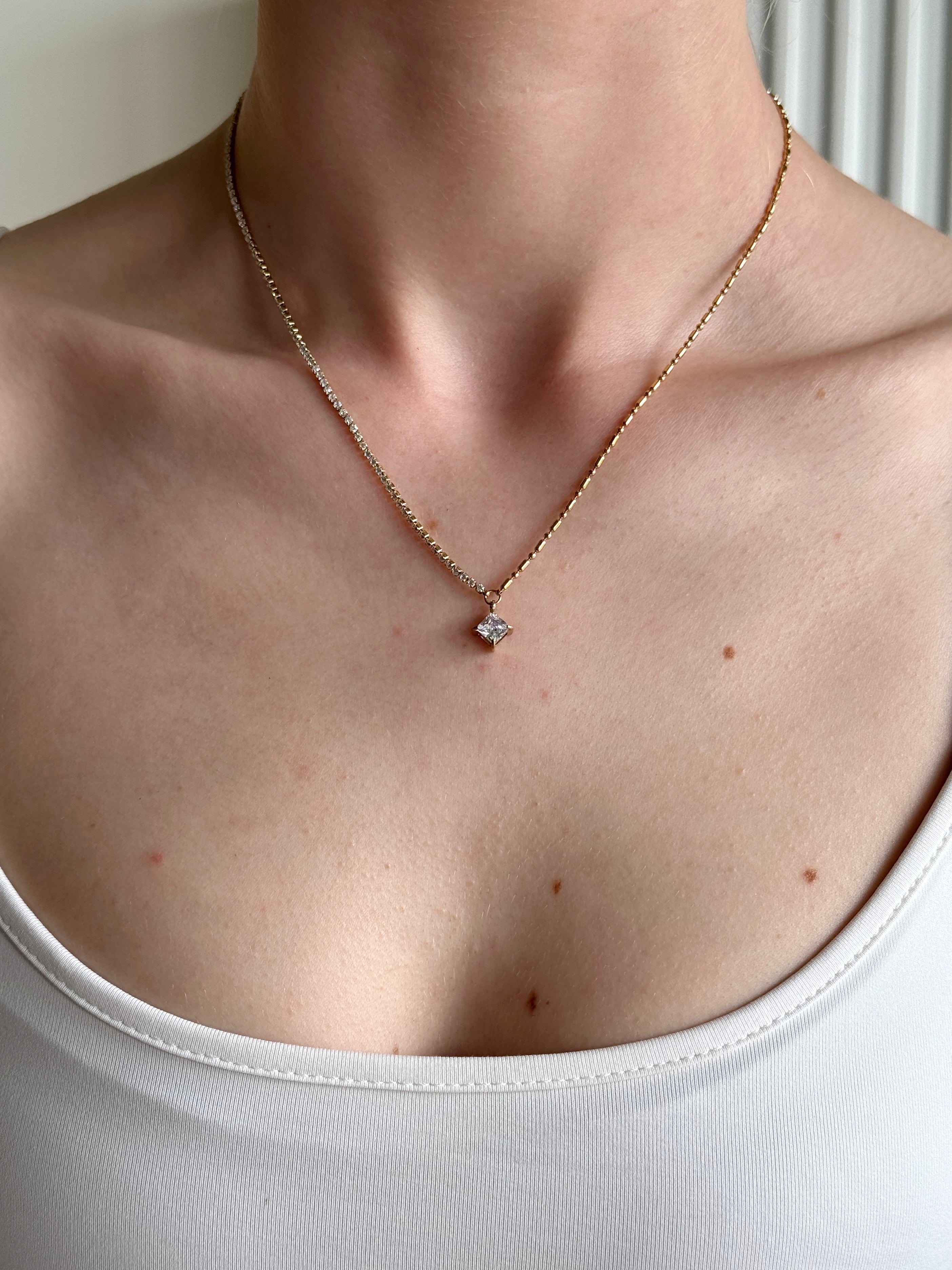 Necklace with a small pendant worn by a person in a white top.