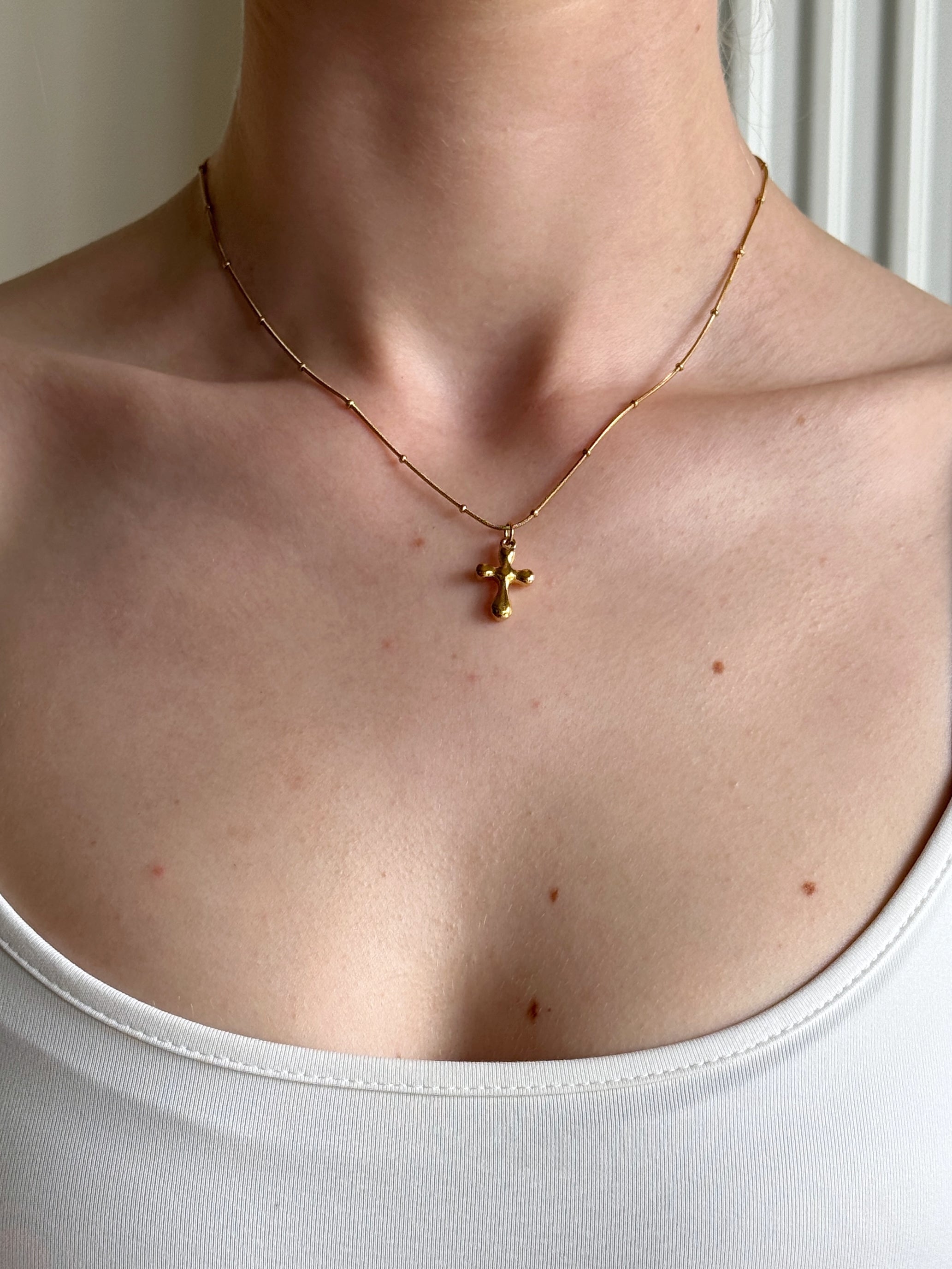Gold necklace with a catholic cross pendant on a person wearing a white tank top.
