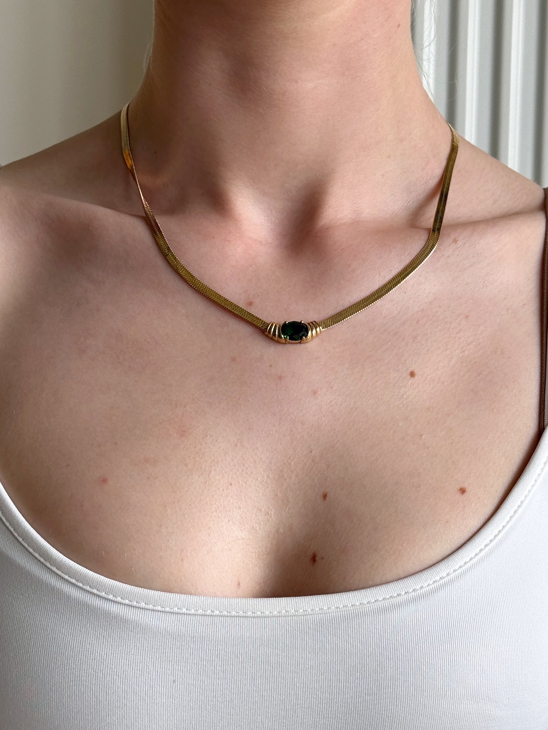 Classy necklace with a green pendant worn by a woman in a white tank top.