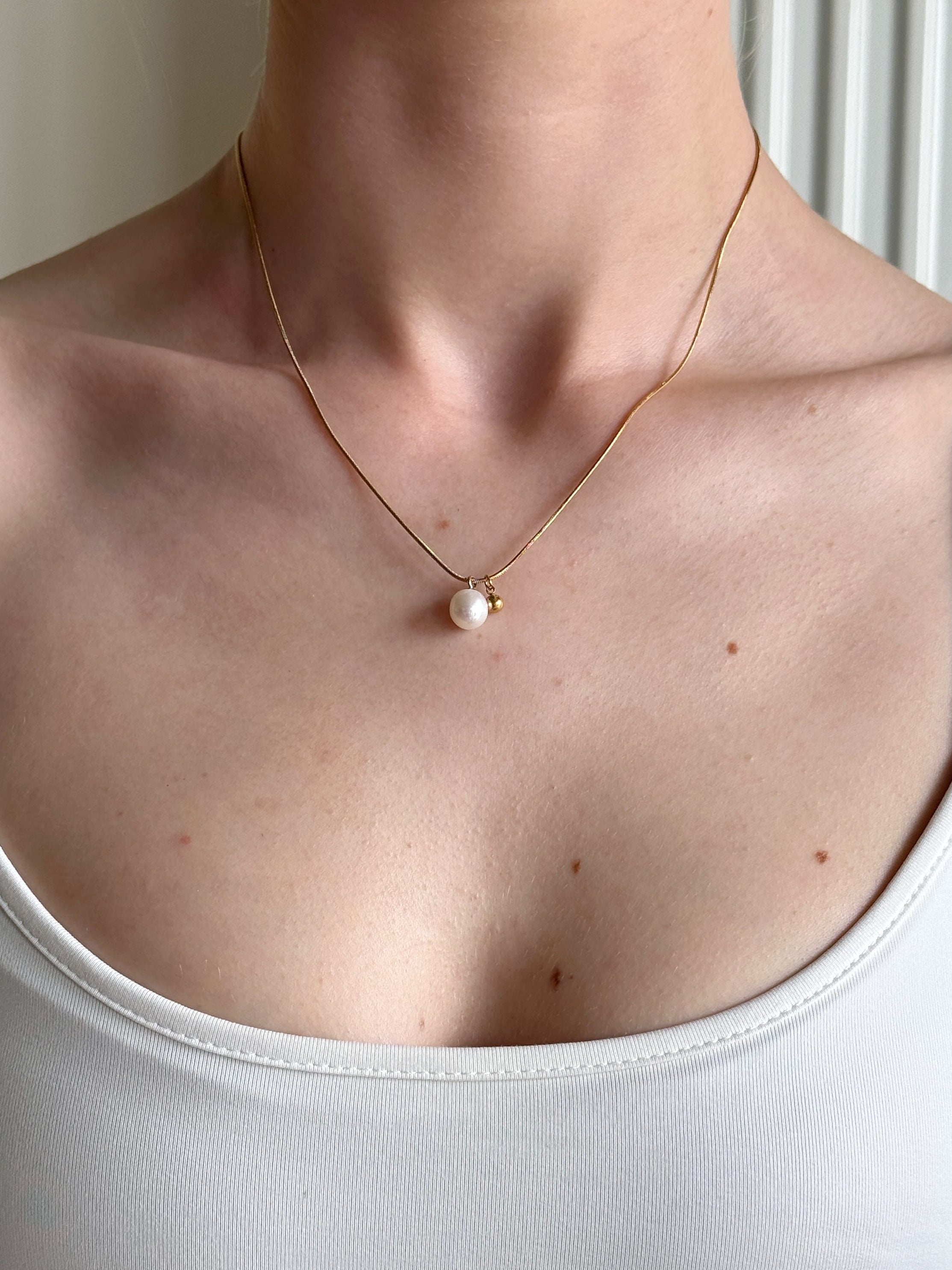 Gold necklace with a pearl pendant on a person wearing a white top.