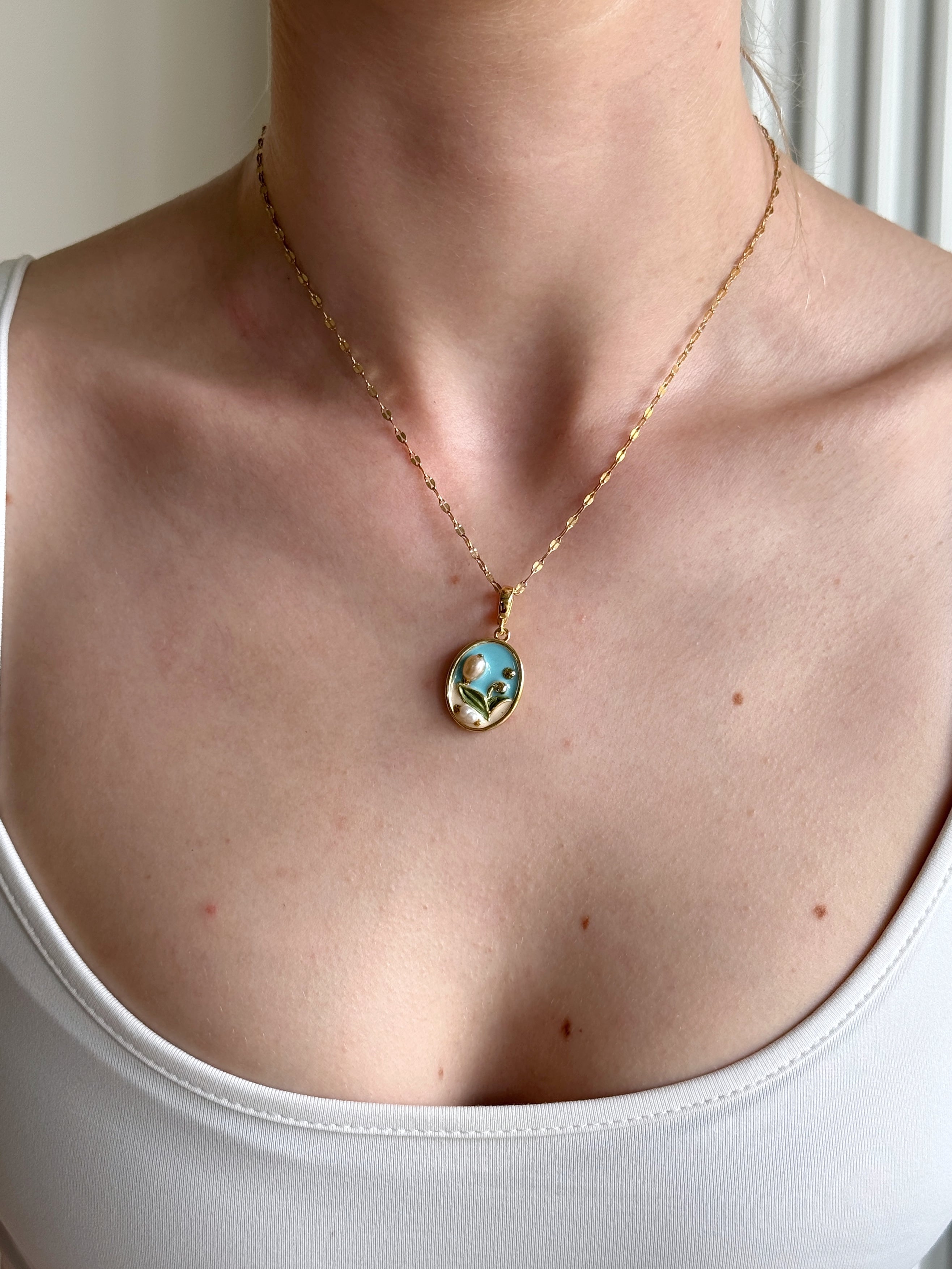 Necklace with a pendant worn by a person in a white top.