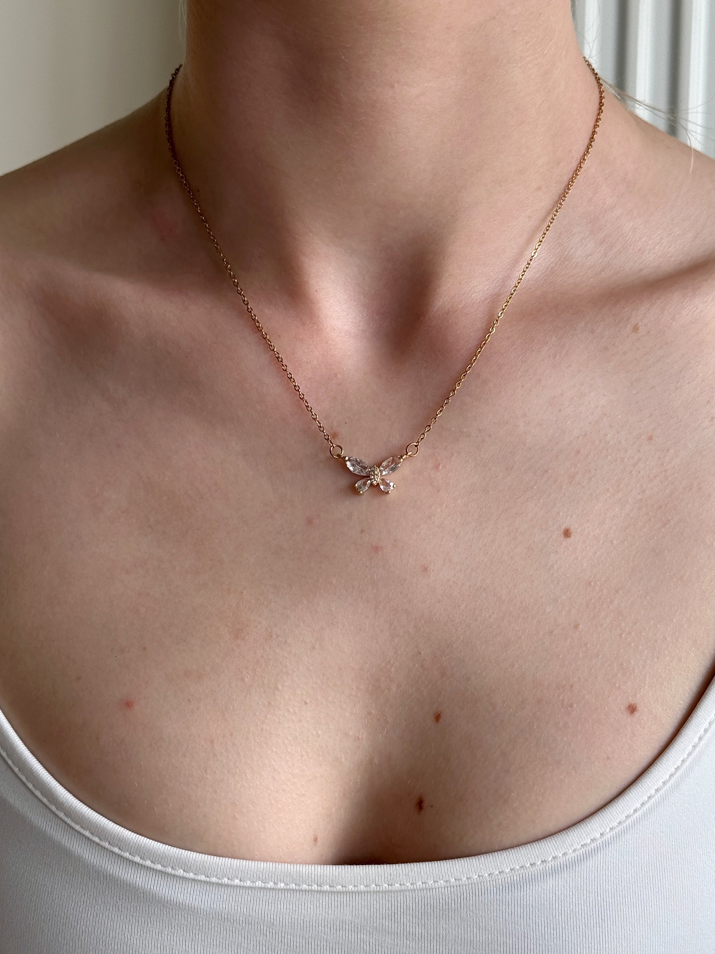 Gold butterfly necklace on a person wearing a white top