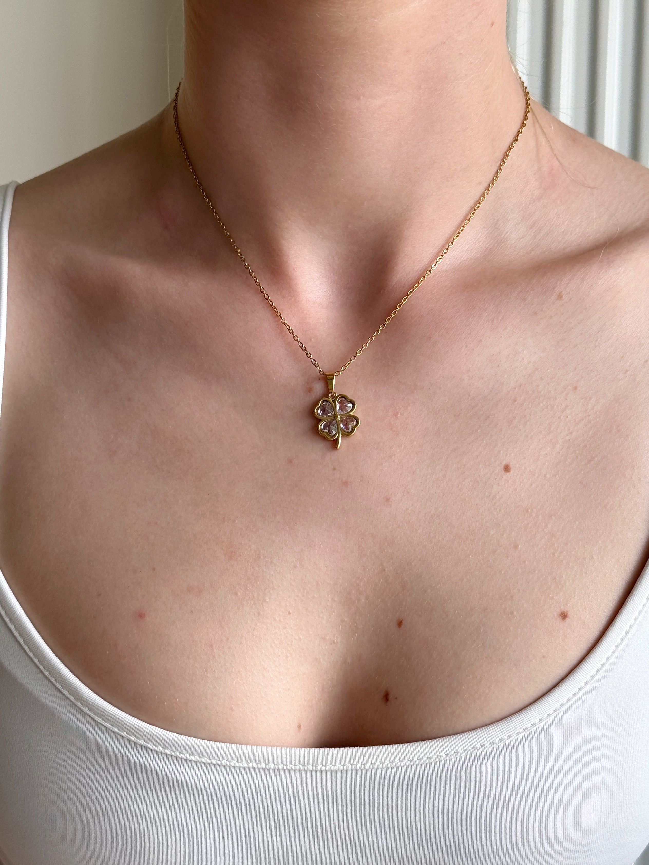 Gold four leaf clover necklace with a pendant on a person wearing a white tank top.