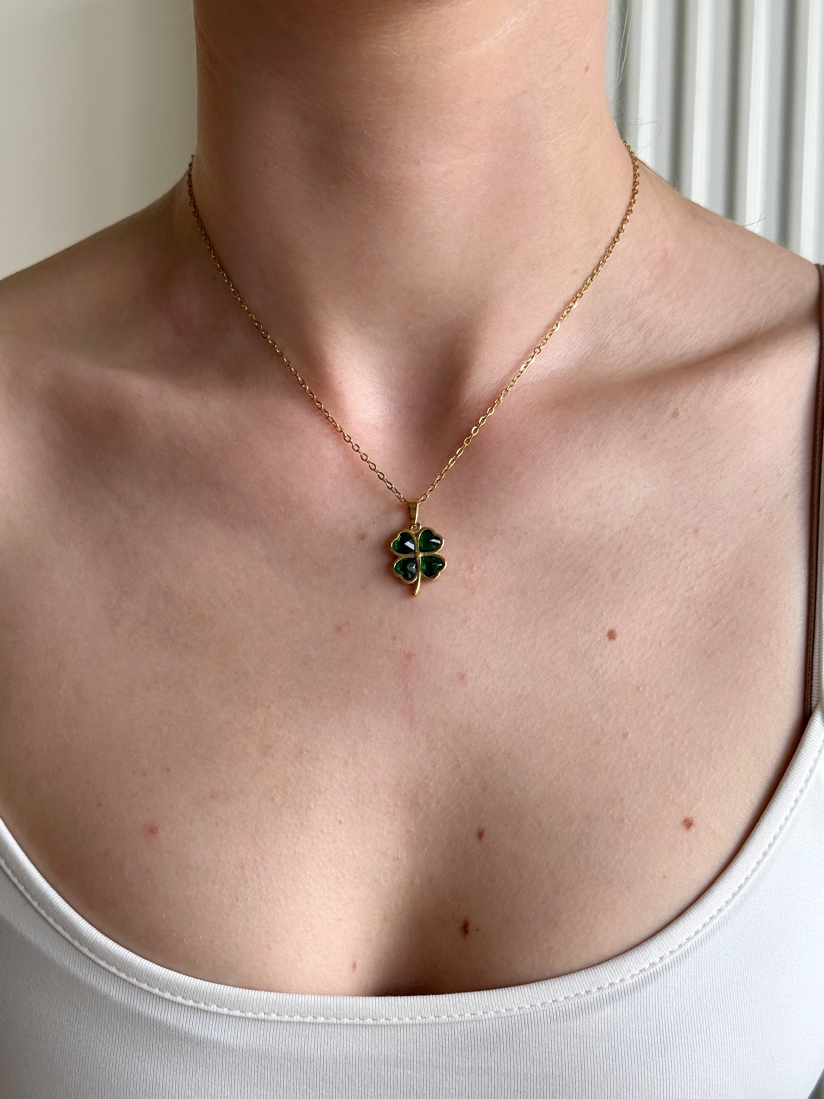 Necklace with a four leafed clover -shaped pendant worn by a person in a white tank top.