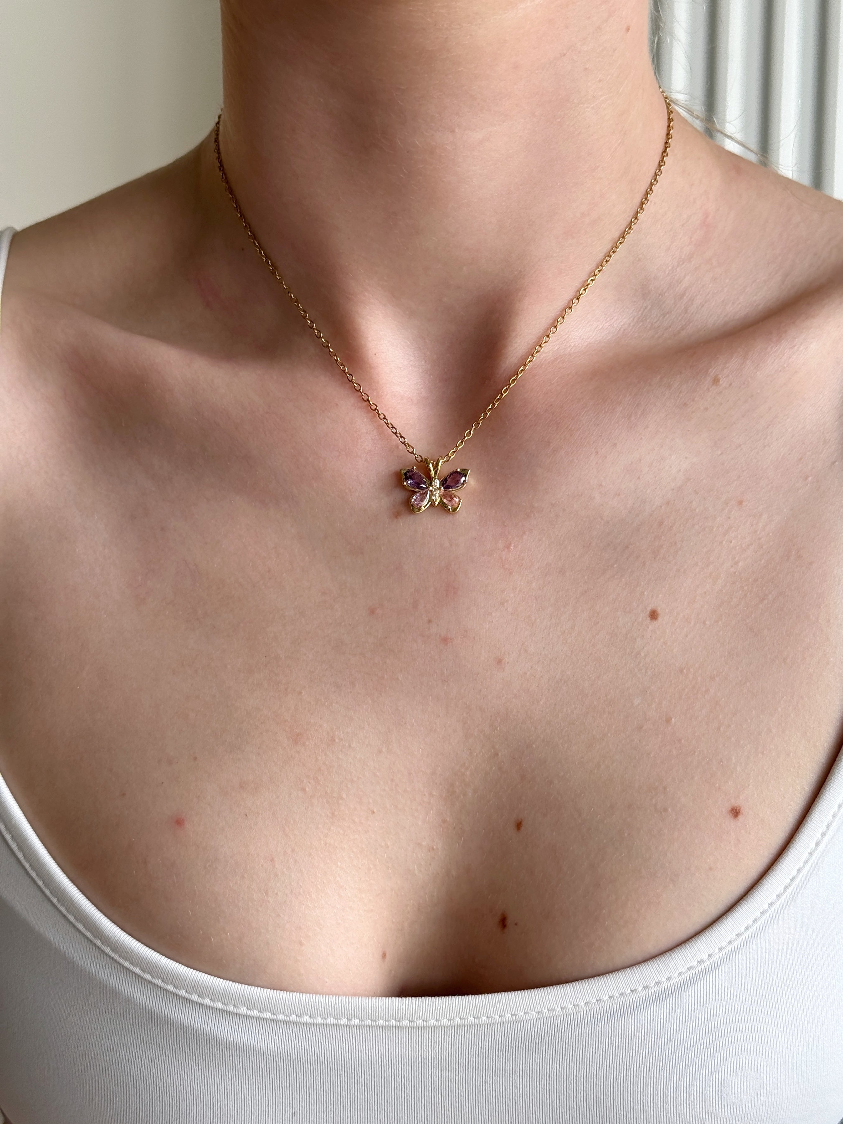 Necklace with a lavender butterfly pendant worn by a person, close-up of the neck and chest area.