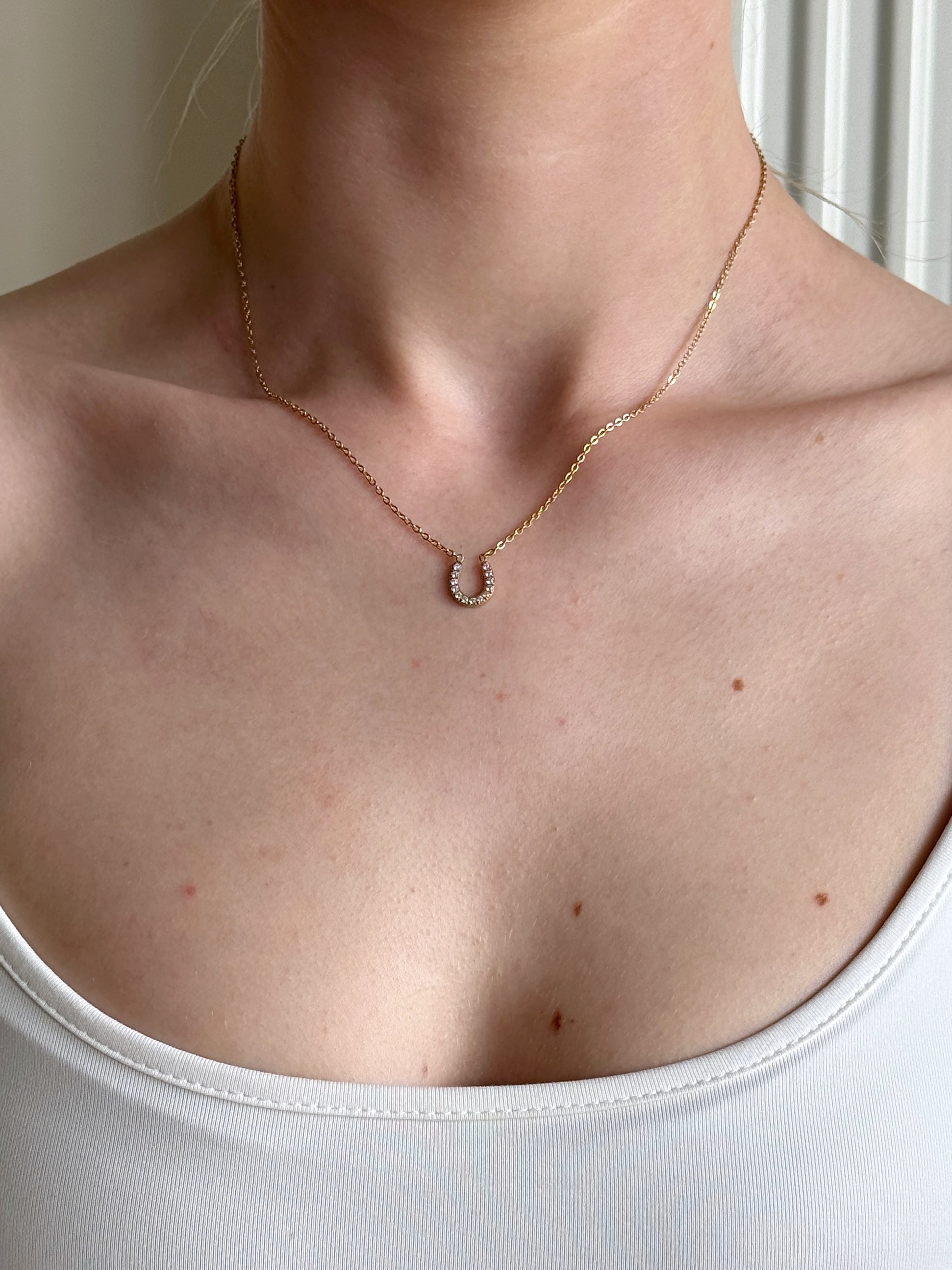 Horseshoe gold necklace on a woman wearing a white top with a neutral background