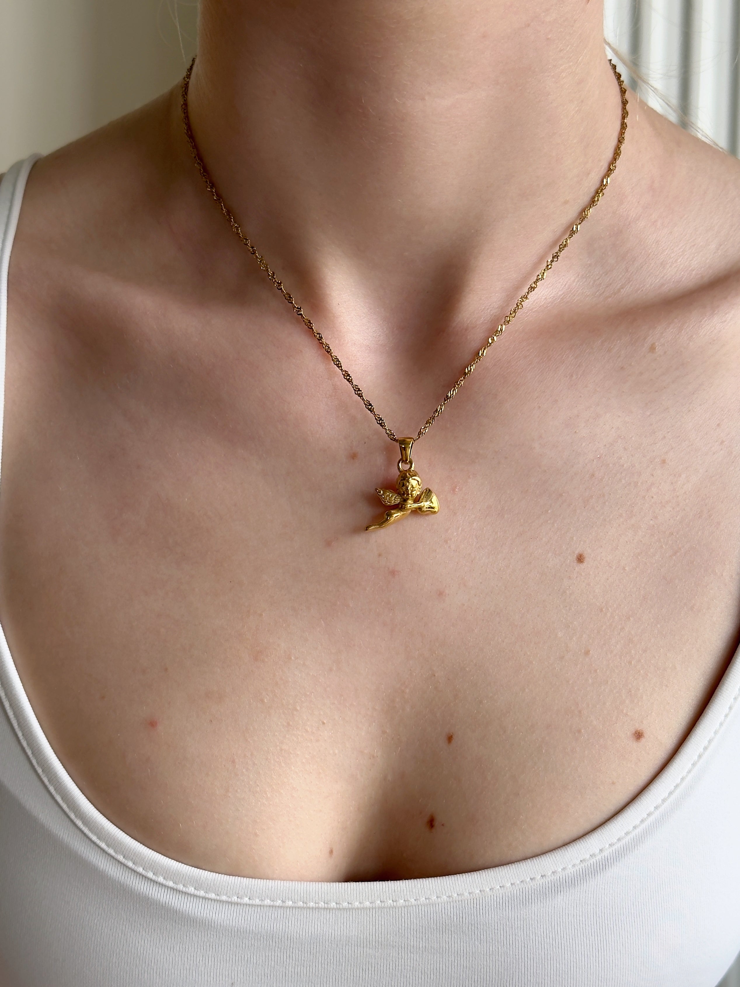 Gold necklace with a cupid love pendant on a person wearing a white tank top.