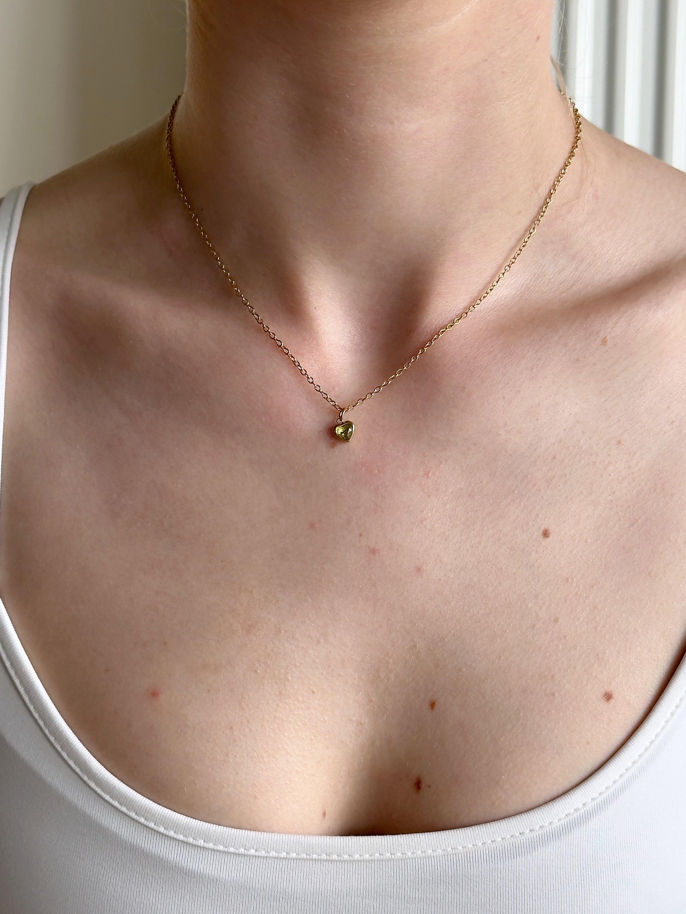 Gold necklace with a small green pendant on a girl wearing a white tank top.