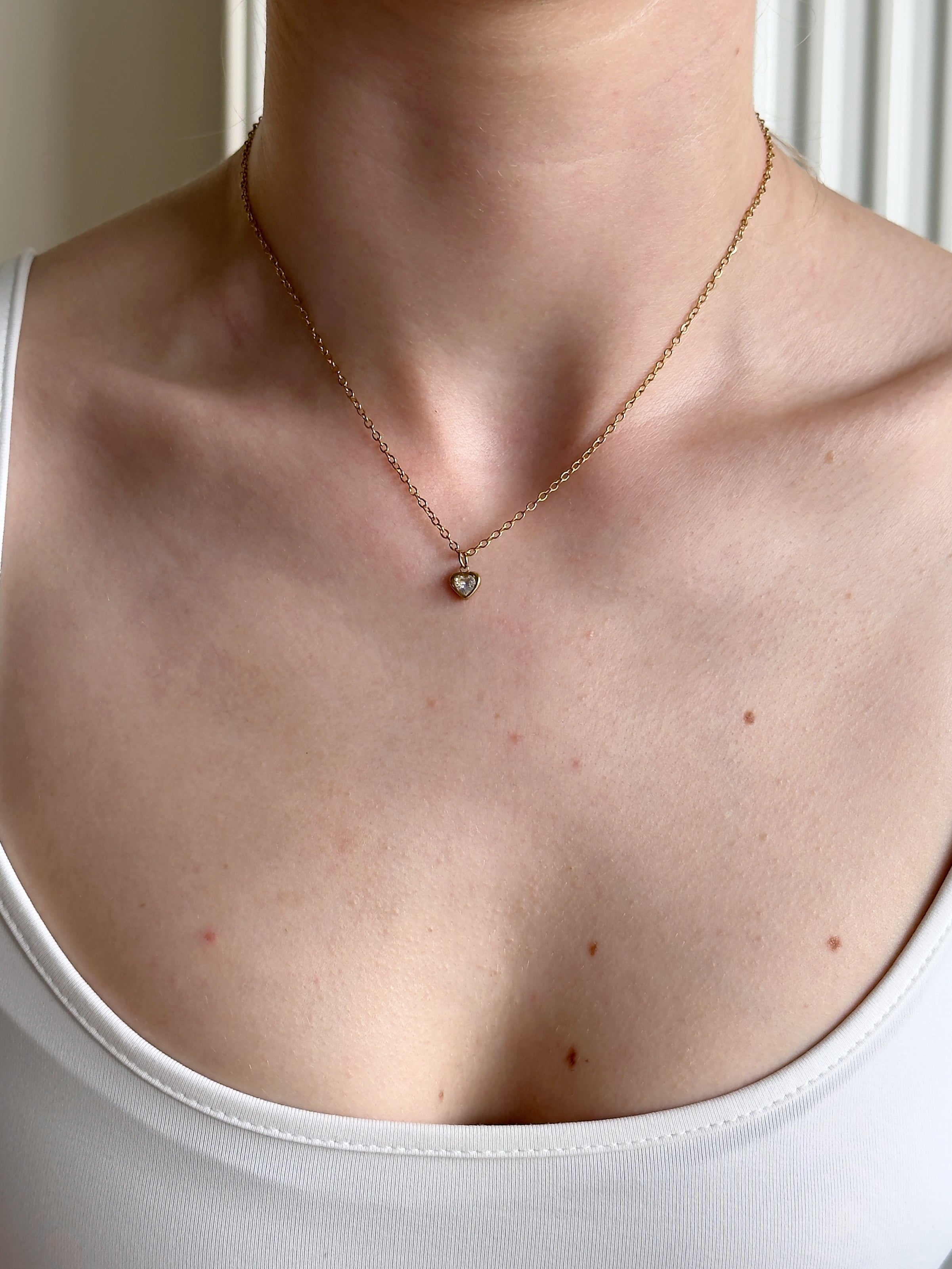 Necklace with a small white heart pendant worn by a person in a white tank top.
