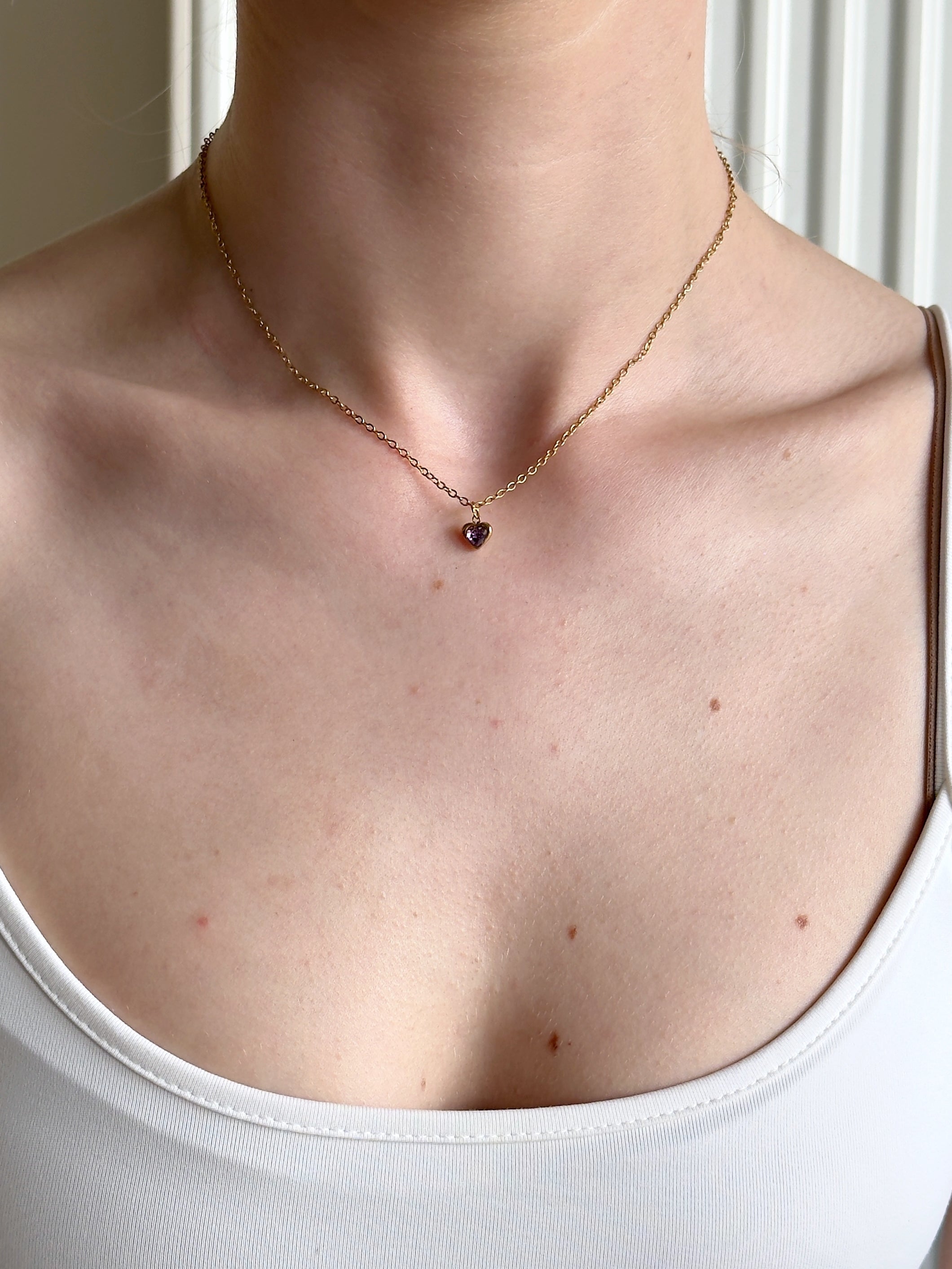 Necklace with a purple heart gemstone on a person wearing a white tank top.