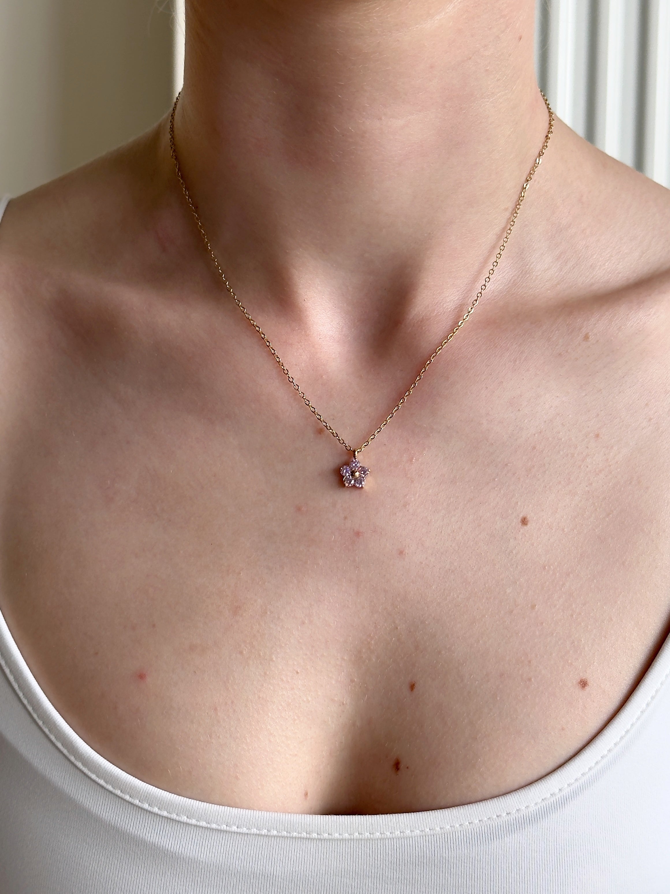 Delicate stainless steel necklace with a pink flower pendant worn by a person