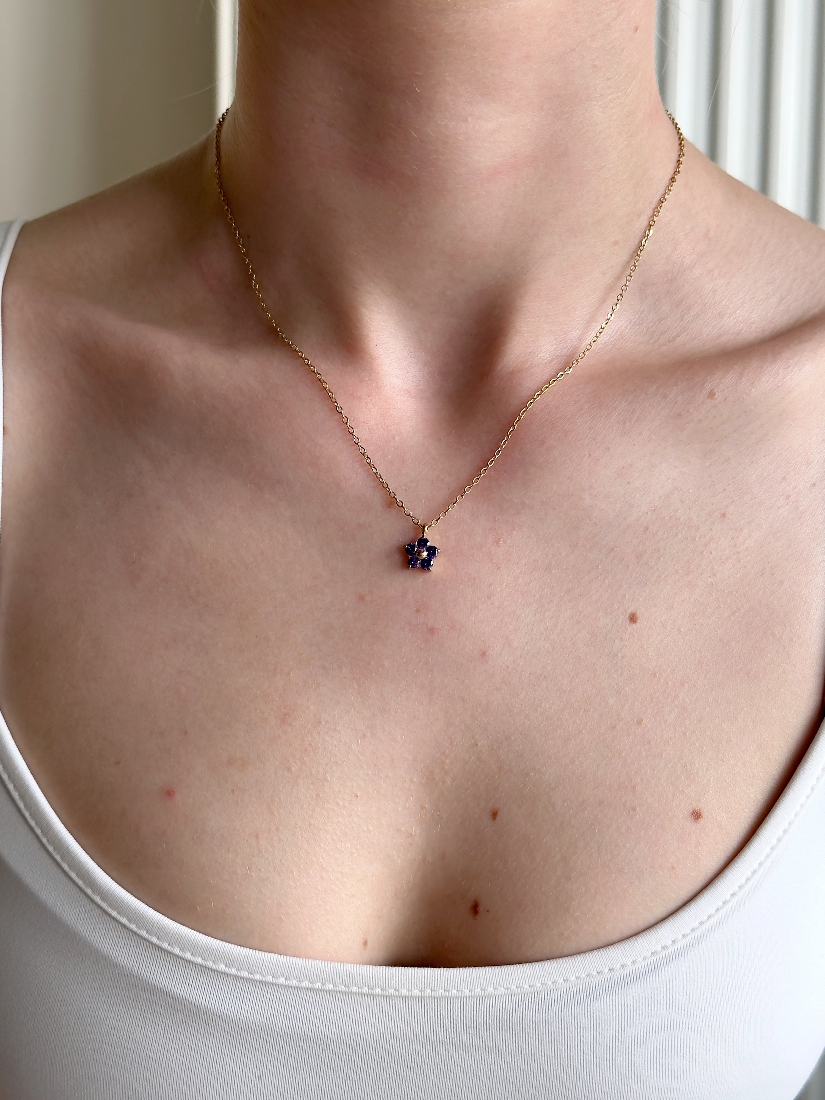 Stainless steel necklace with a small purple pendant worn by a person in a white top.