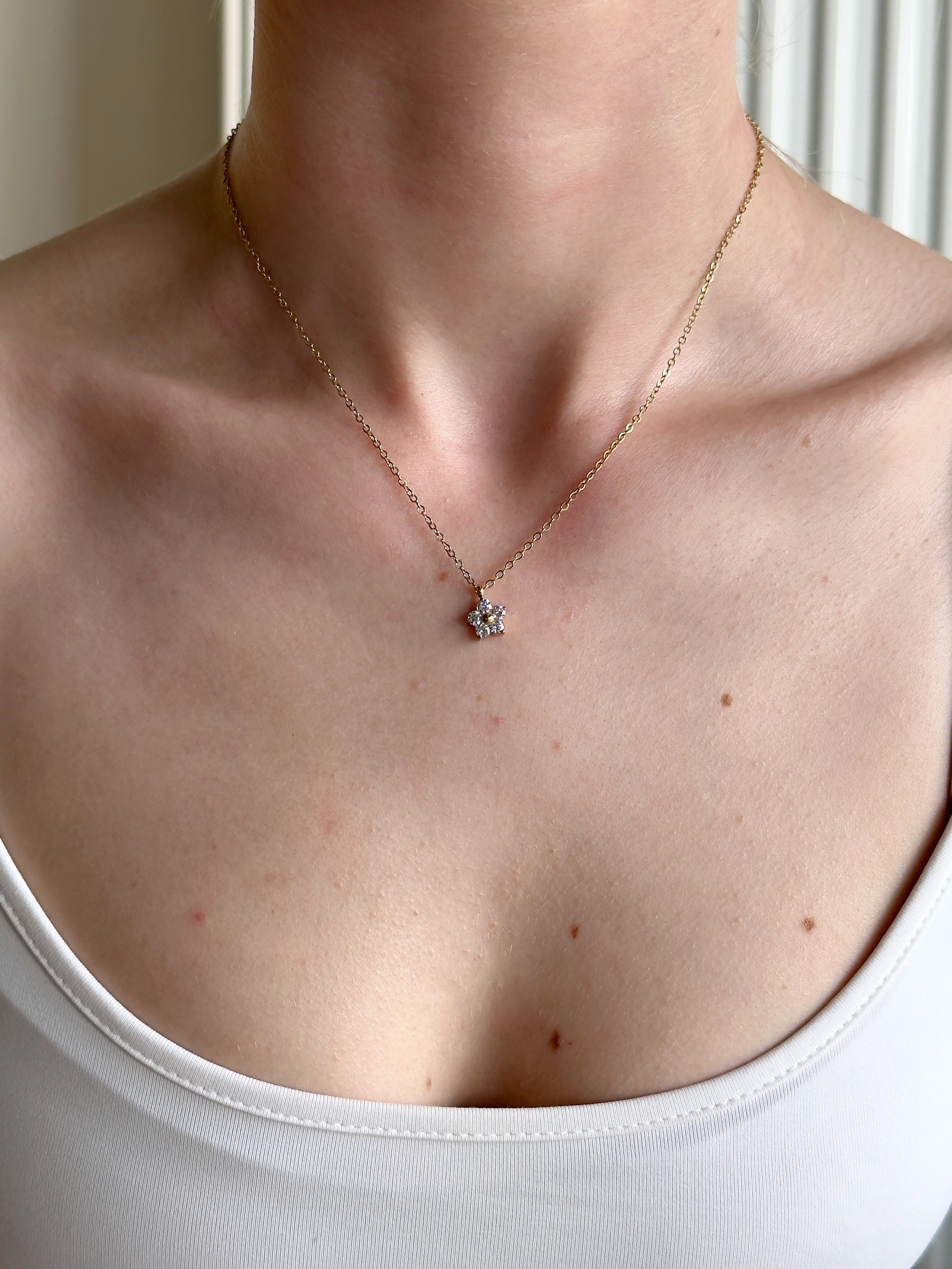 Gold waterproof necklace with a small flower pendant worn by a woman in a white top.