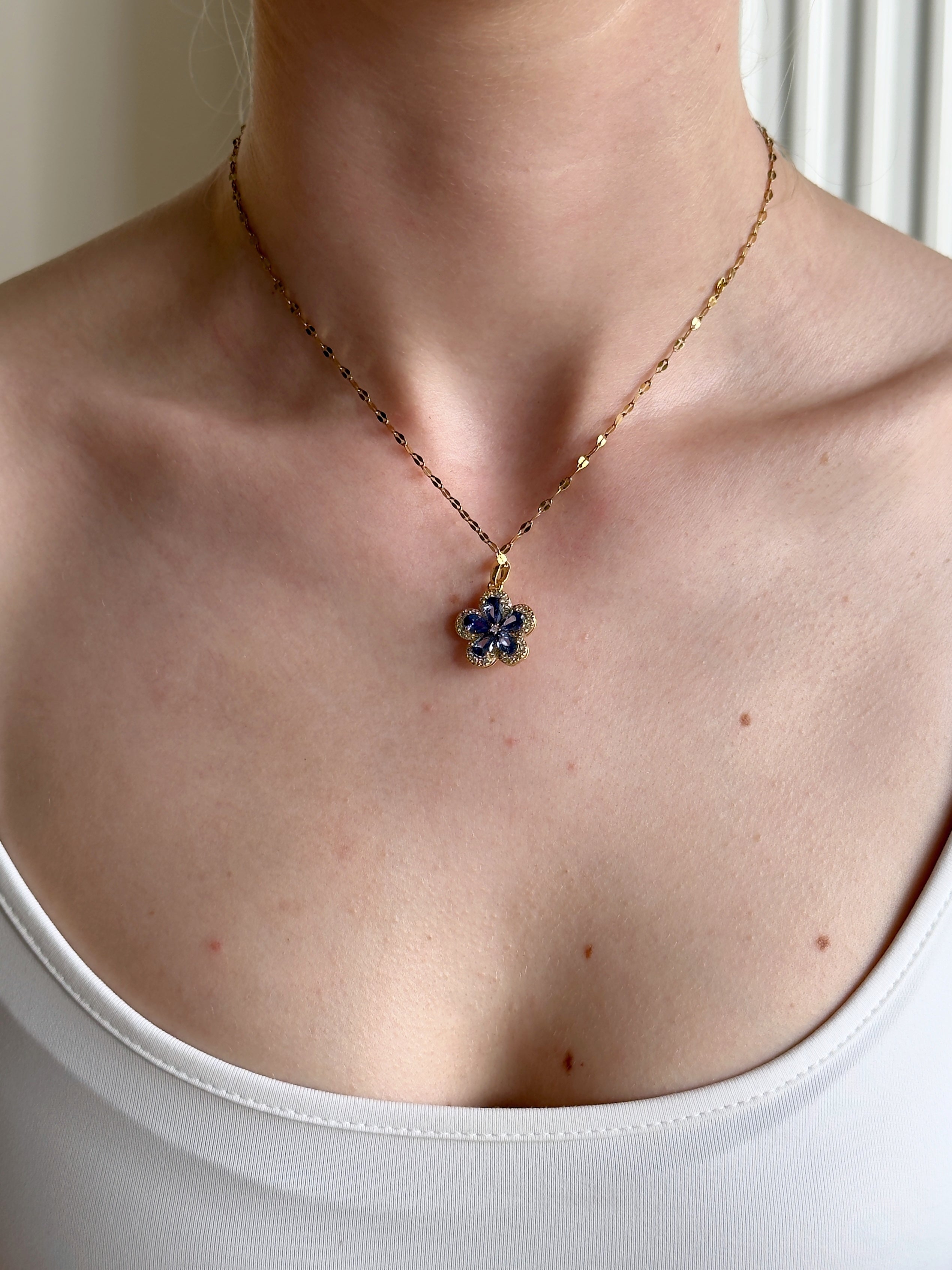 Necklace with a sapphire blue floral pendant worn by a person