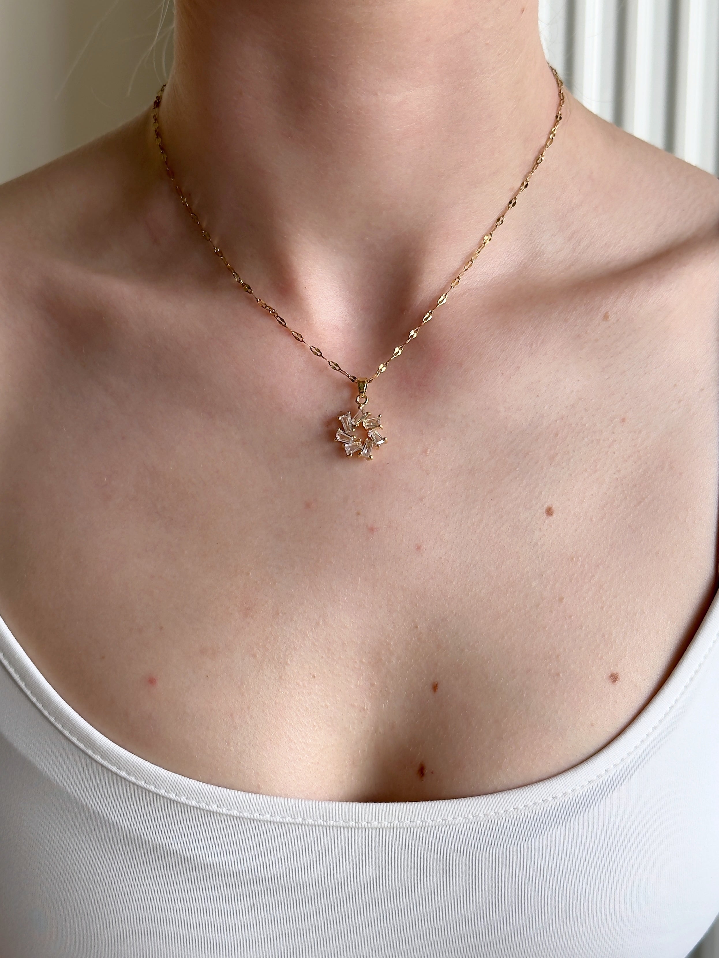 Necklace with a floral pendant worn by a person against a neutral background