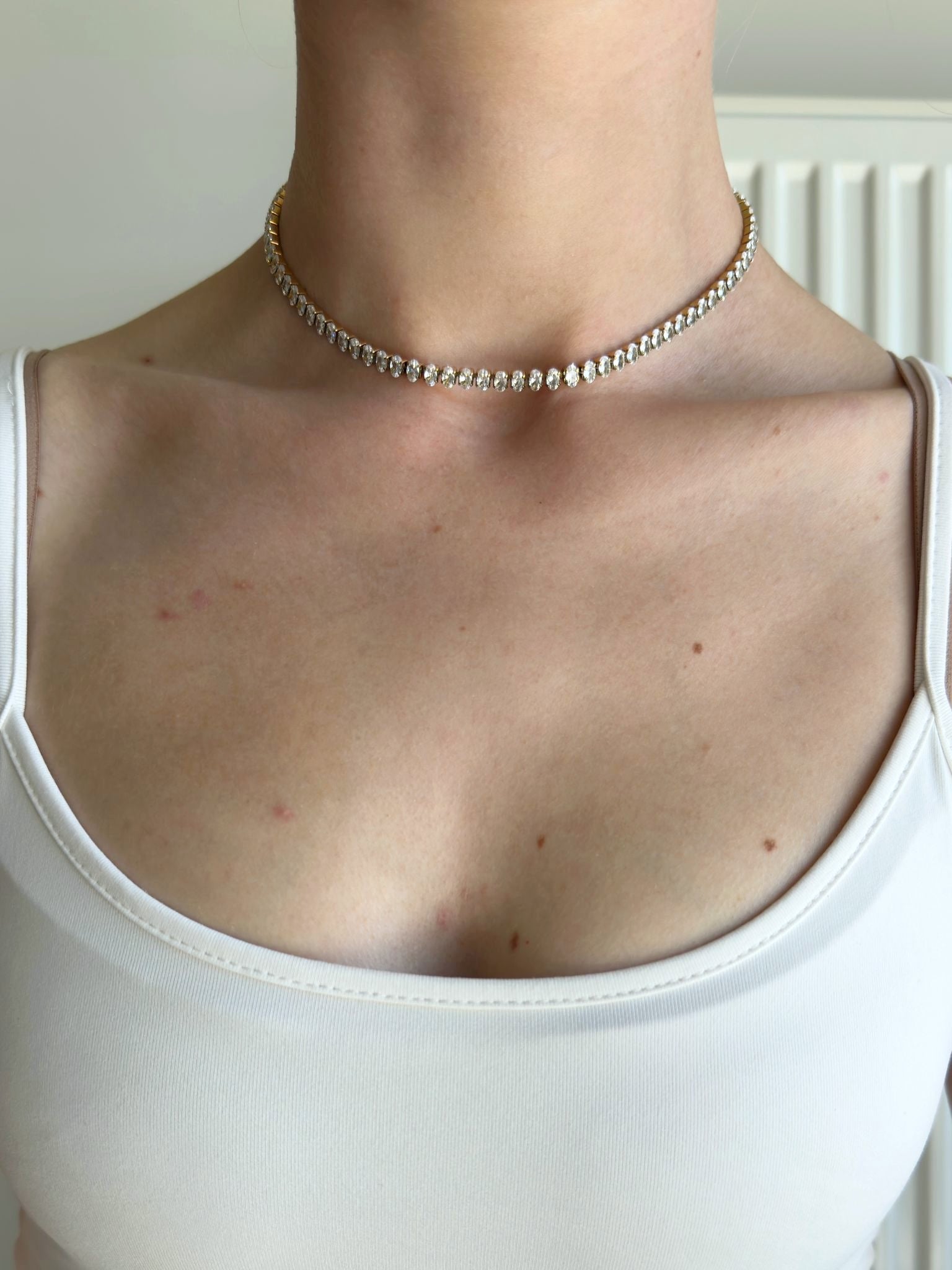 Necklace on a person wearing a white tank top against a neutral background