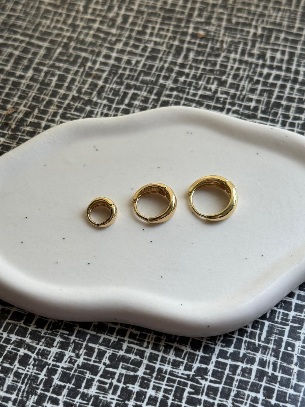 Three classic gold rings in different sizes on a white ceramic dish with a textured black and white background
